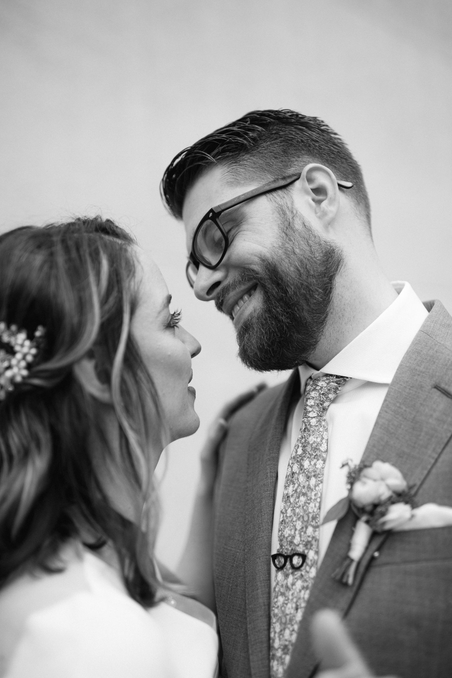 Full length black and white portrait of newlyweds against minimal wall background.