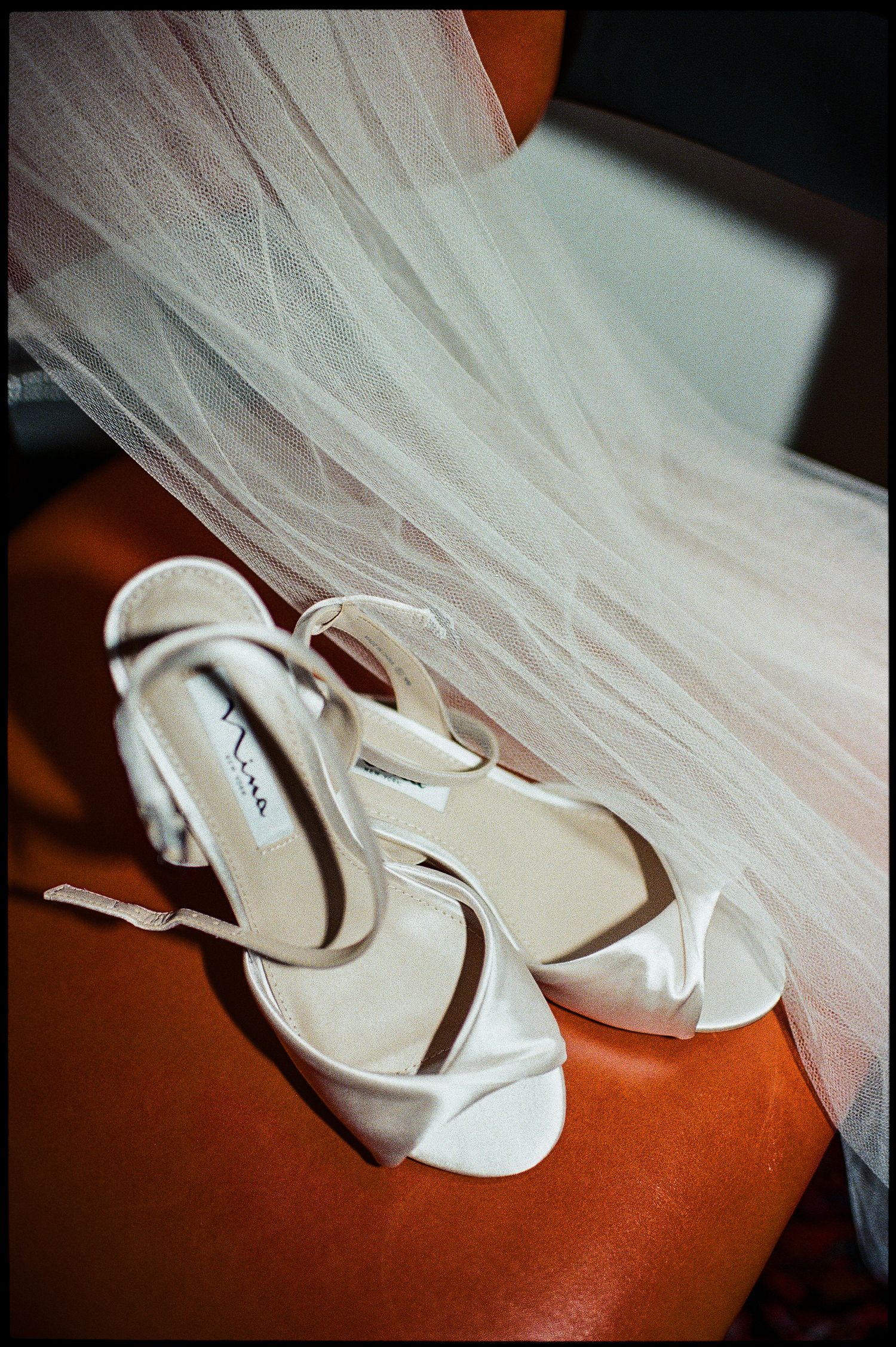 White strappy wedding heels placed next to delicate tulle veil on orange surface.