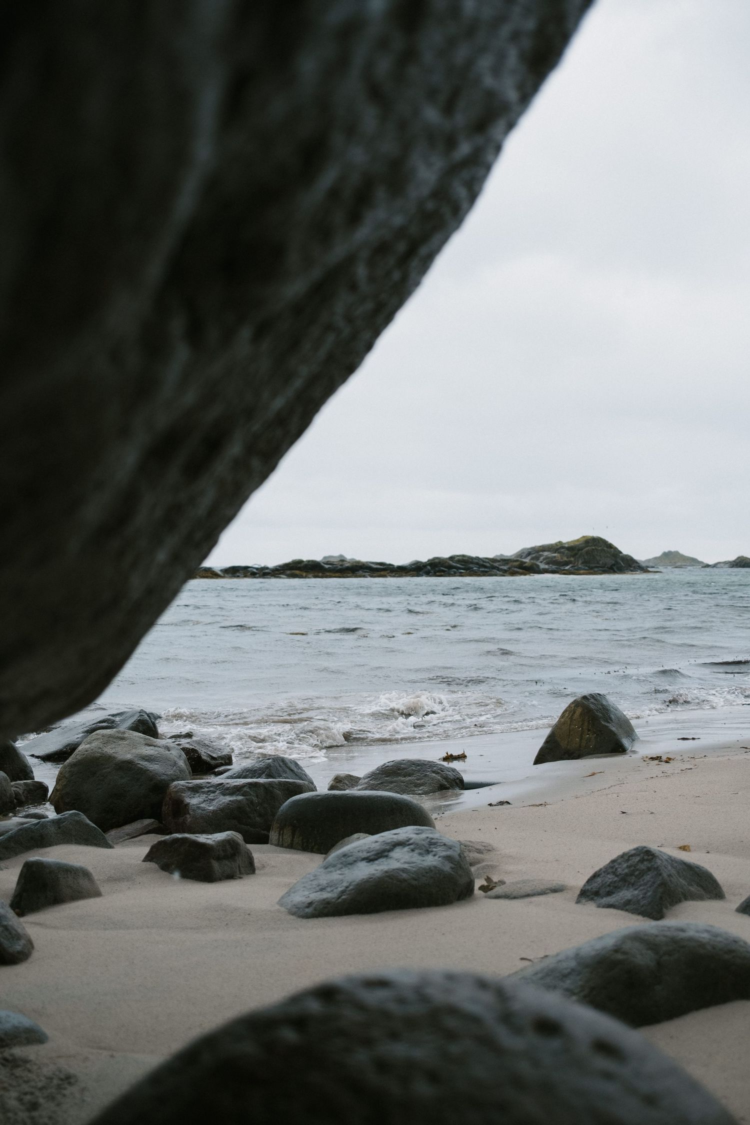 Rocky beach shore with volcanic stones and distant islands viewed through natural rock frame.