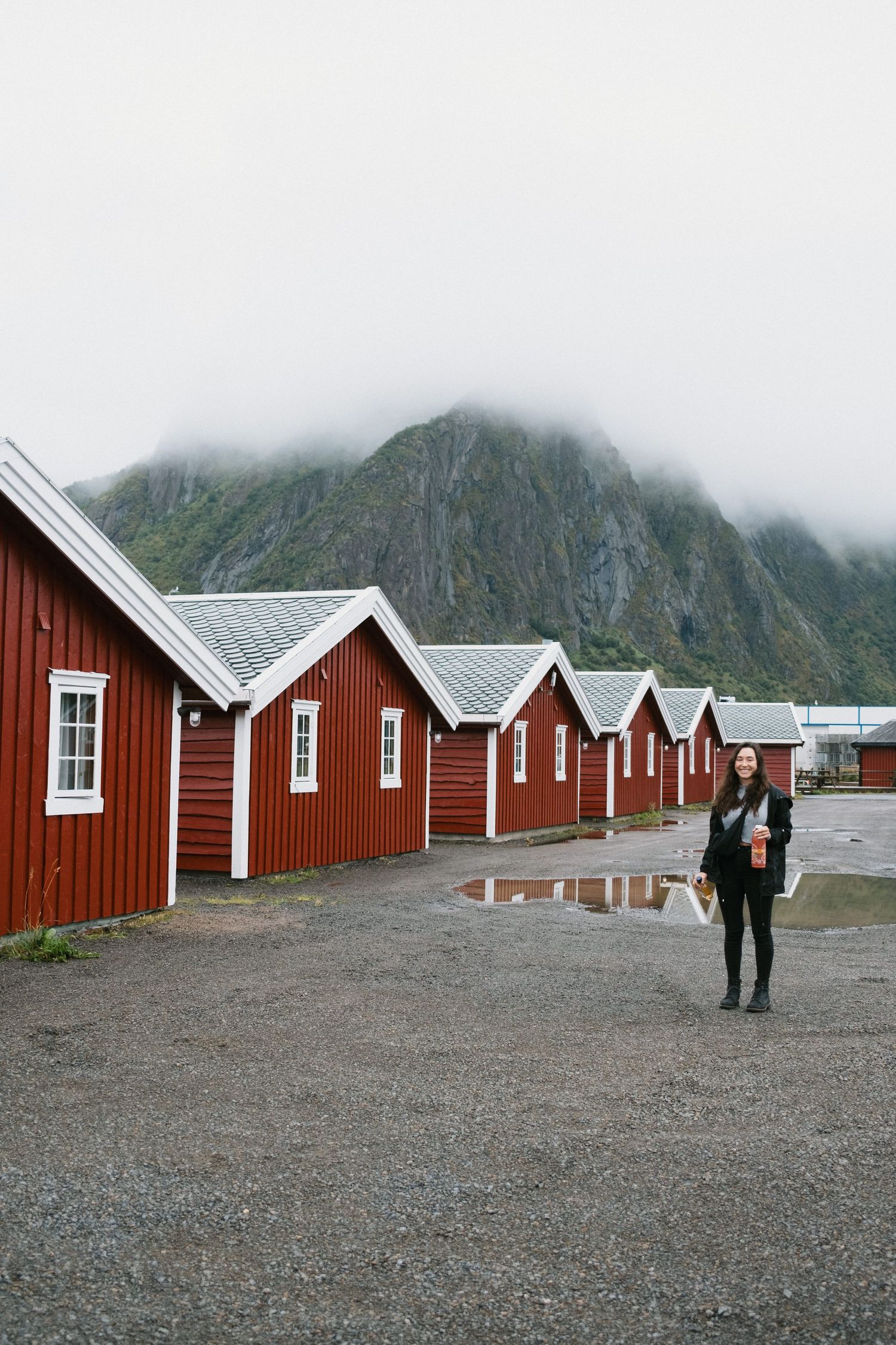 Row of identical red wooden cabins against a dramatic mountain backdrop in Norway.