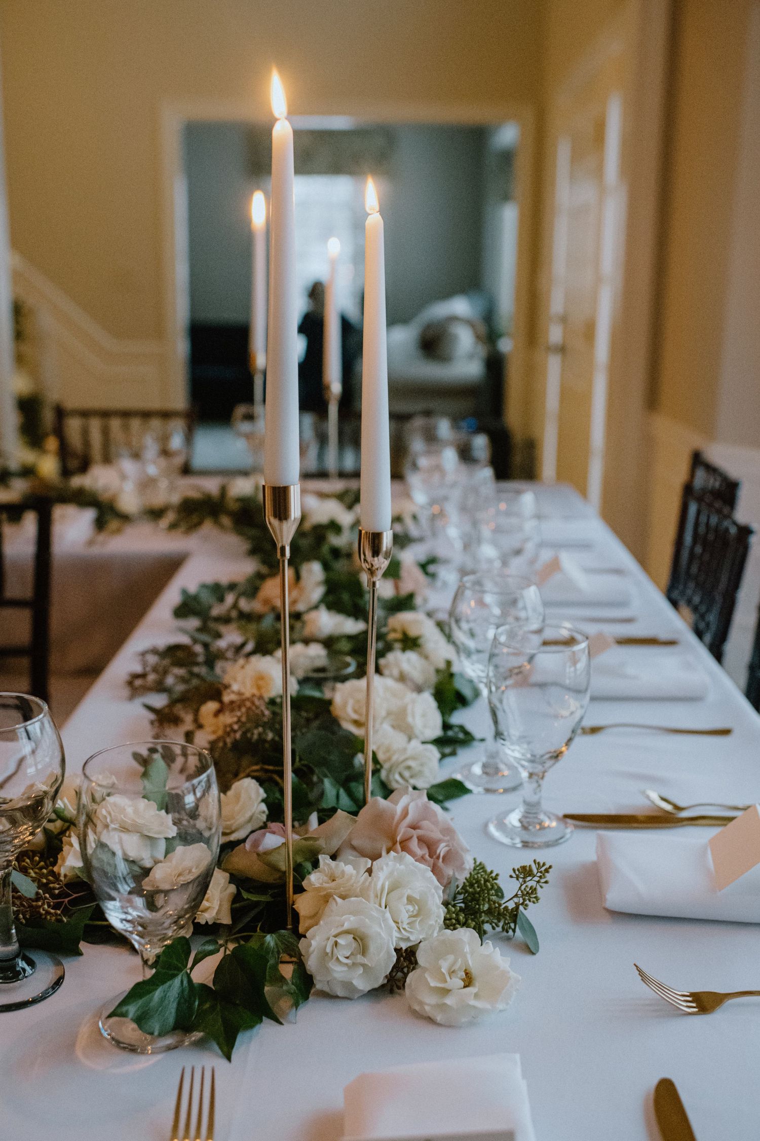 A wedding reception table with tall white candles and romantic floral centerpieces.