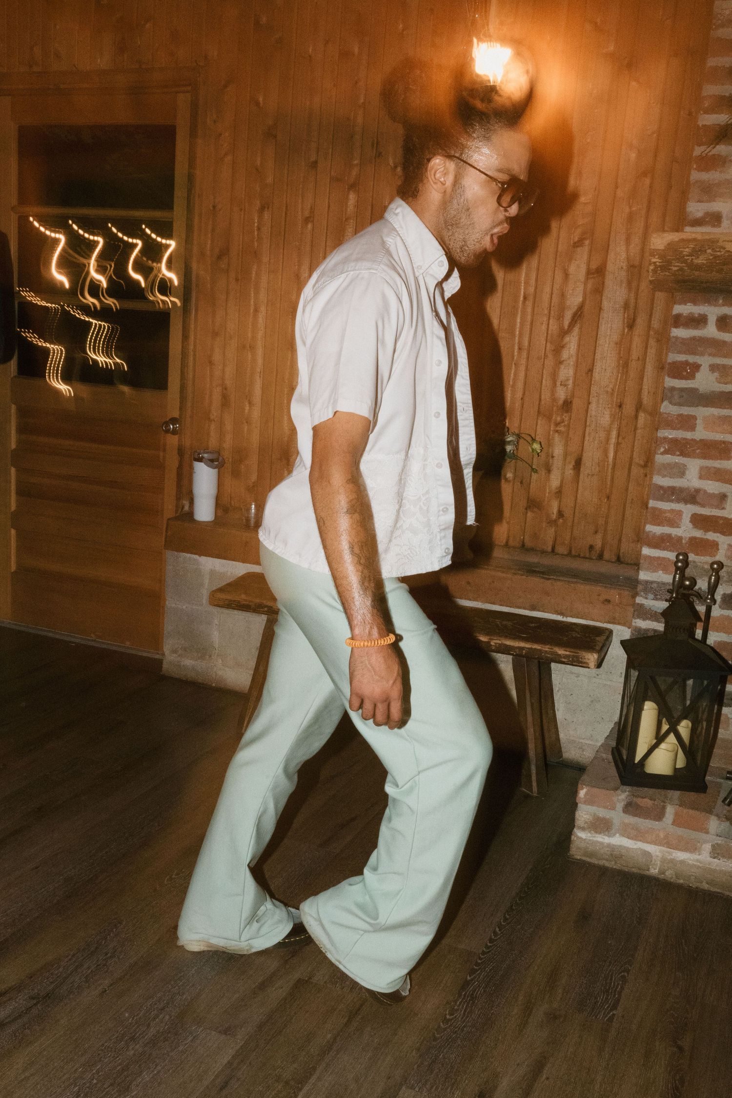 Wedding guest dancing solo on wooden floor in rustic venue with brick wall.
