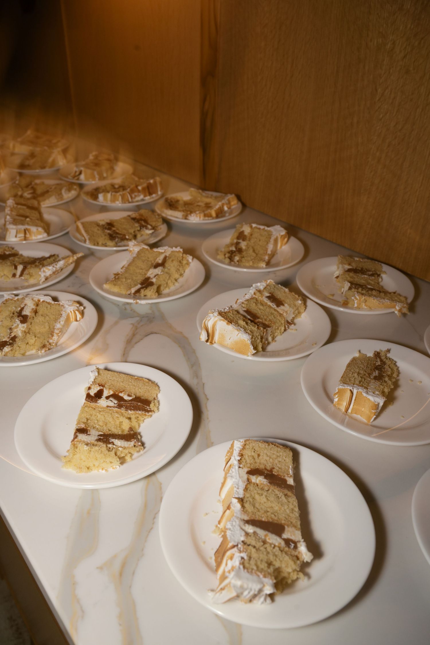 Multiple plates of layered white wedding cake slices arranged on white dishes.