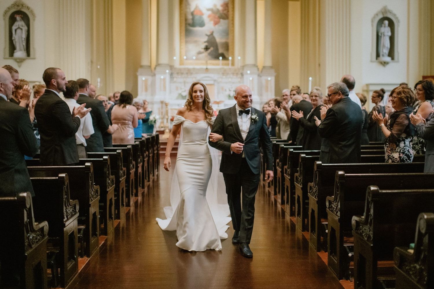 Joyous recessional down church aisle with guests standing and celebrating.