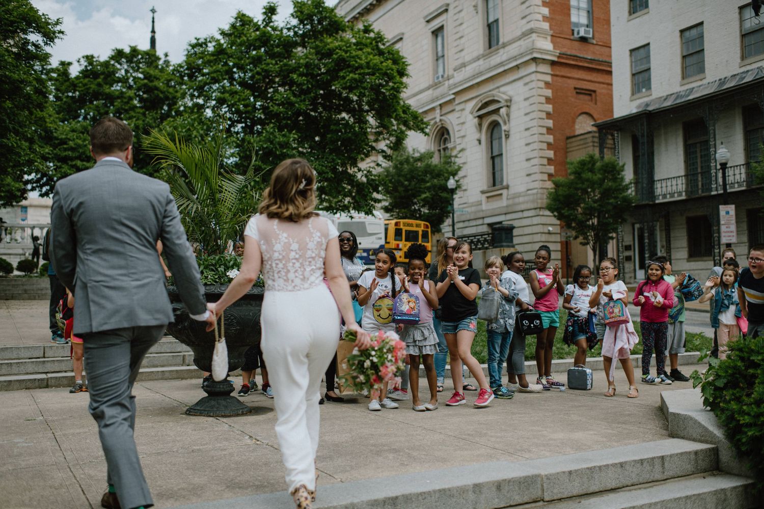 bride and groom walk by group of cheering school children in baltimore