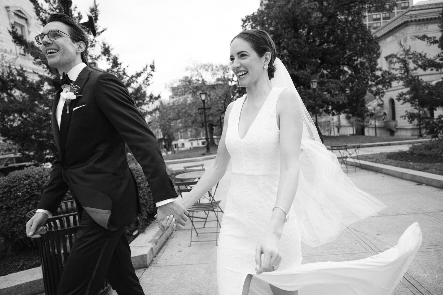 A black and white photo of a couple in wedding attire walking outdoors while holding hands.