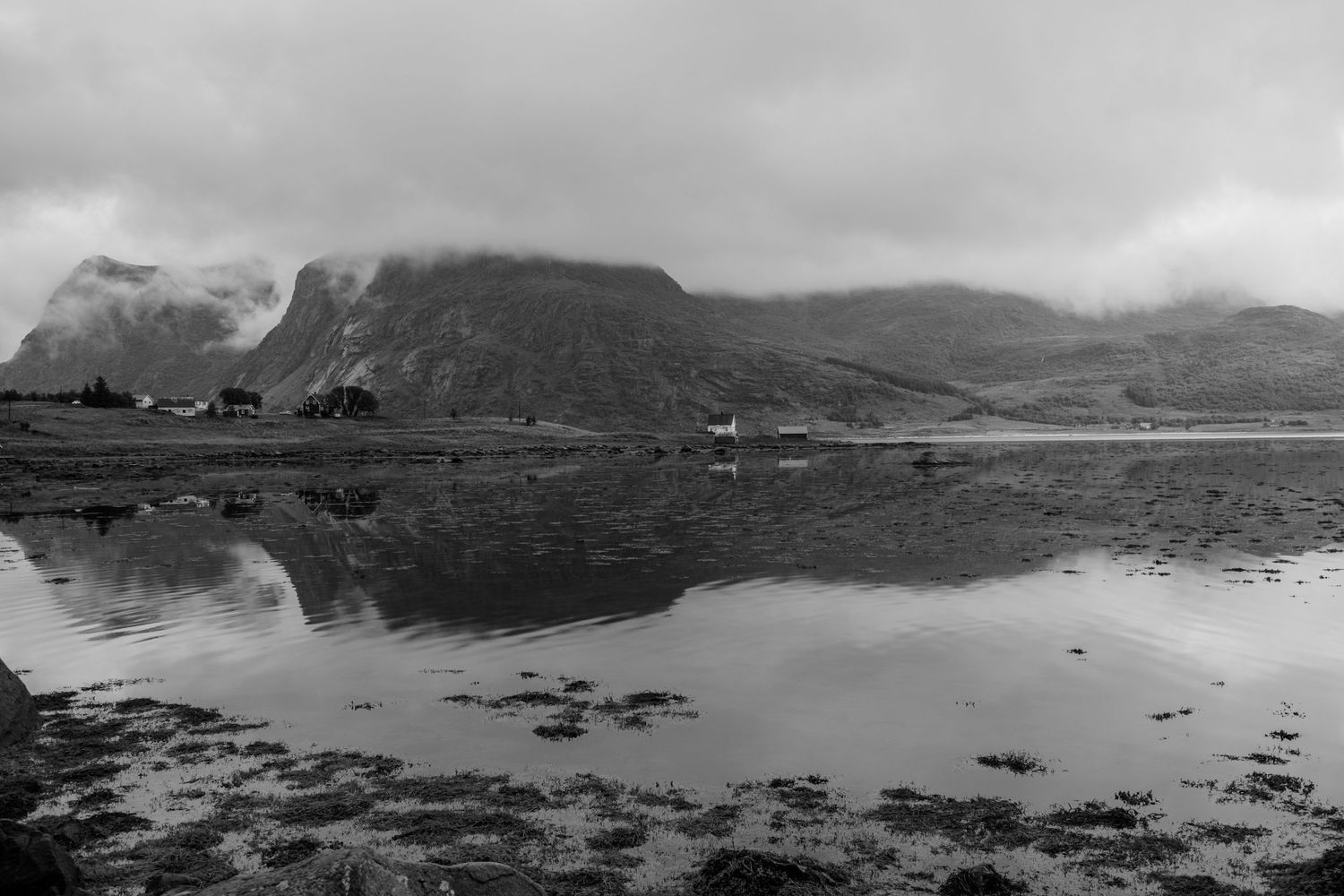 Mountain landscape reflected in calm waters of Norwegian fjord in black and white.