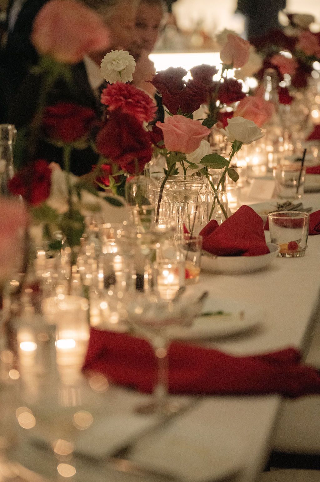 Elegant table settings with red floral centerpieces and glowing candlelight create a romantic dining atmosphere.