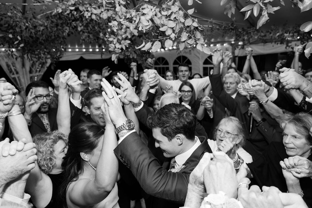 Wedding guests dance together in a joyful crowd at an outdoor reception celebration.