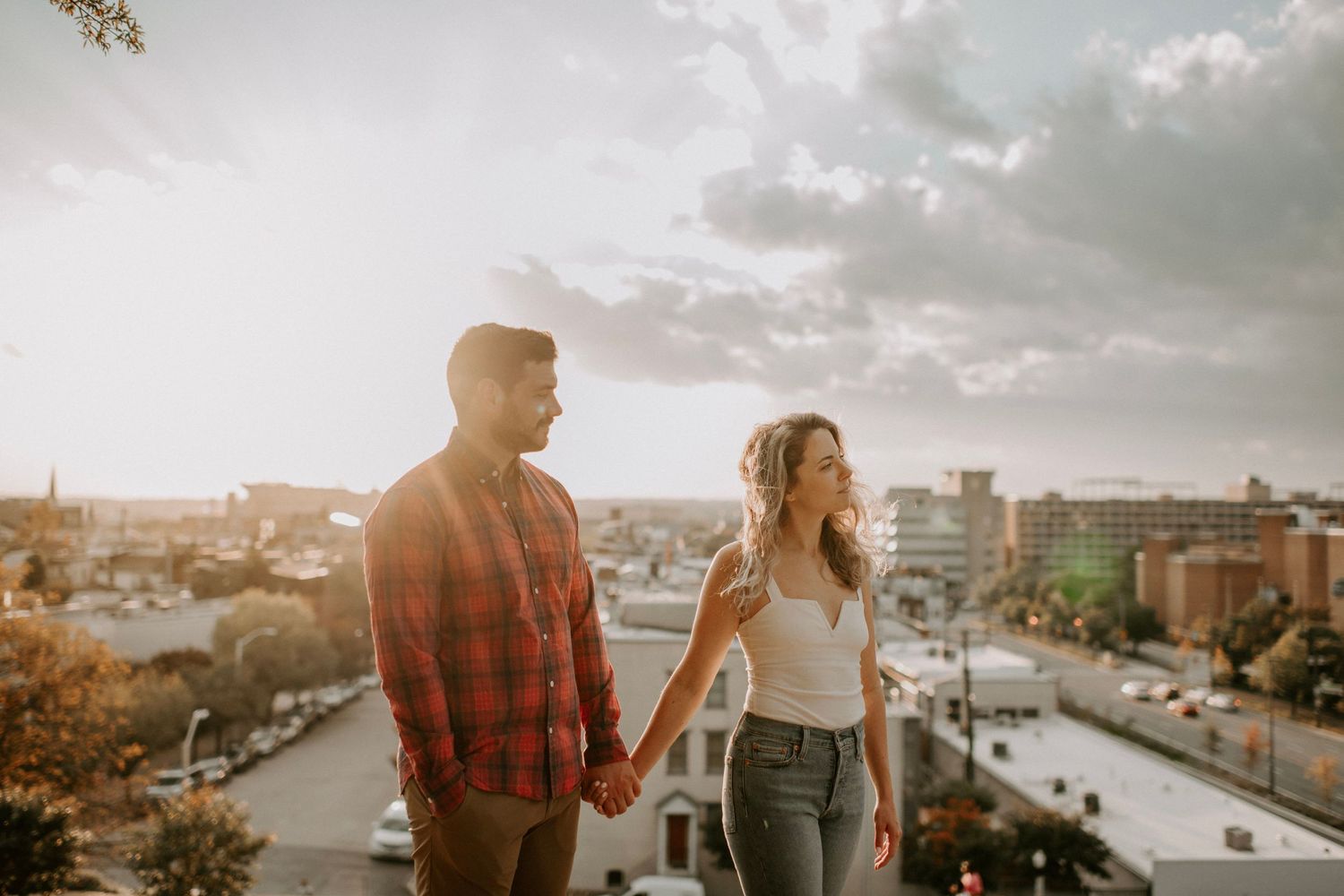 Couple in casual attire holding hands while overlooking city panorama at dusk.