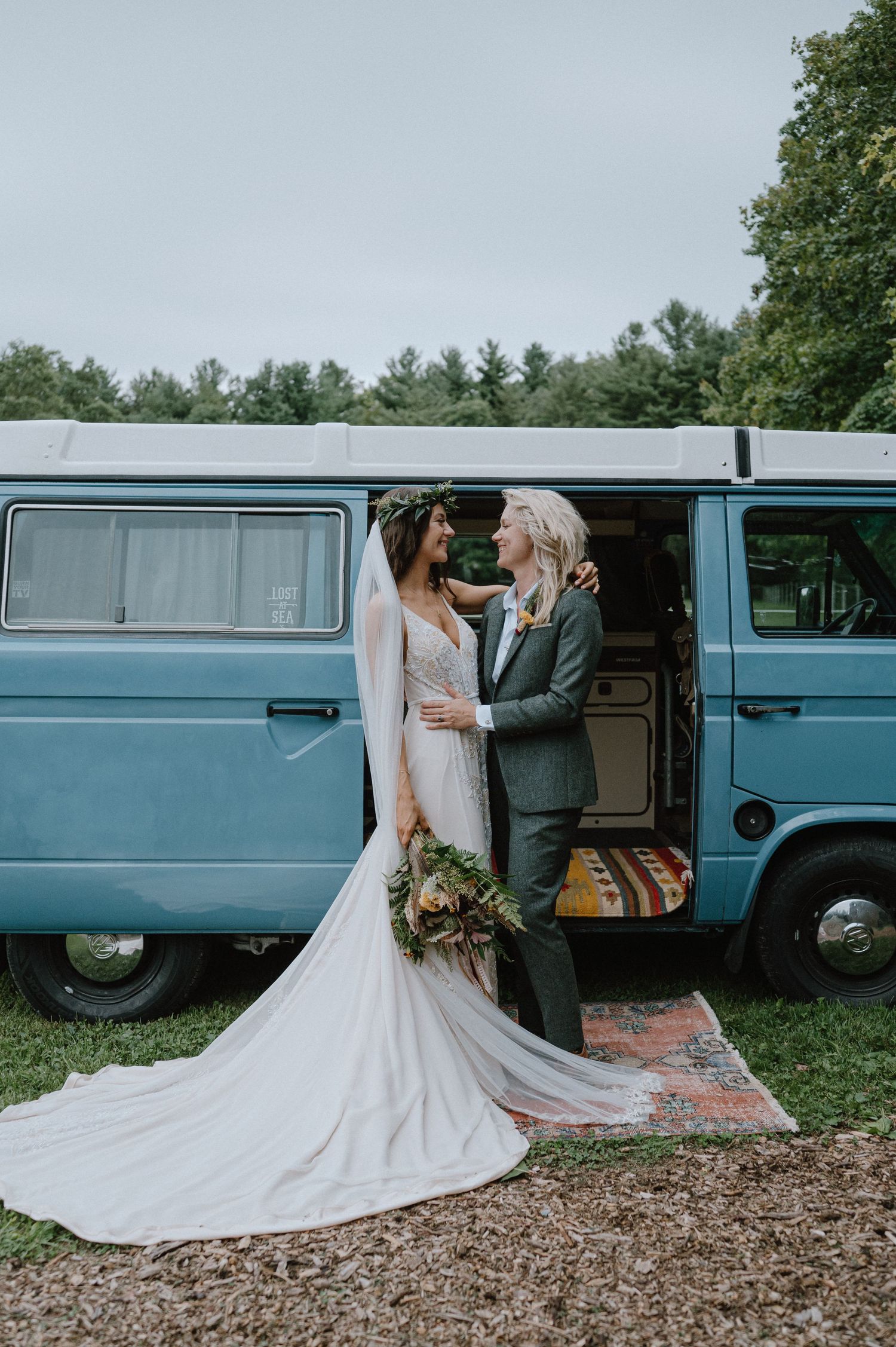 A couple poses in front of a blue vintage VW van, with a flowing white wedding dress.