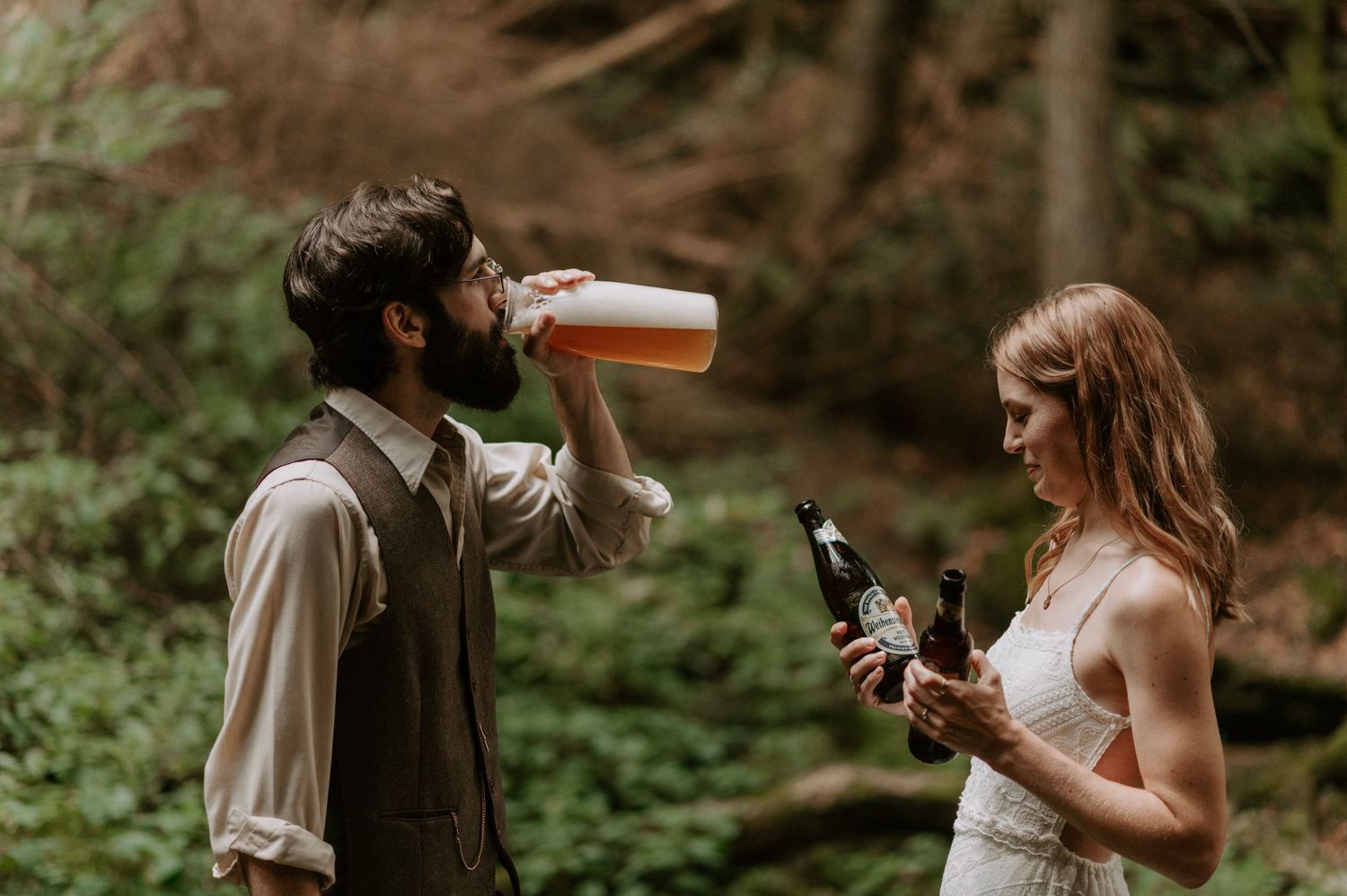 A couple enjoys beverages together during their woodland wedding photoshoot.