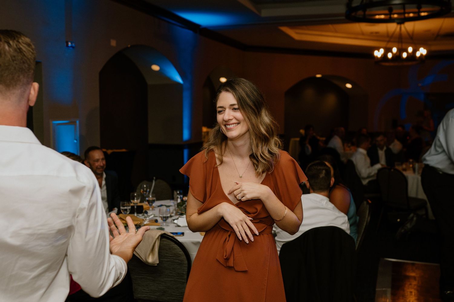 Guest in rust-colored dress laughing during reception celebration.