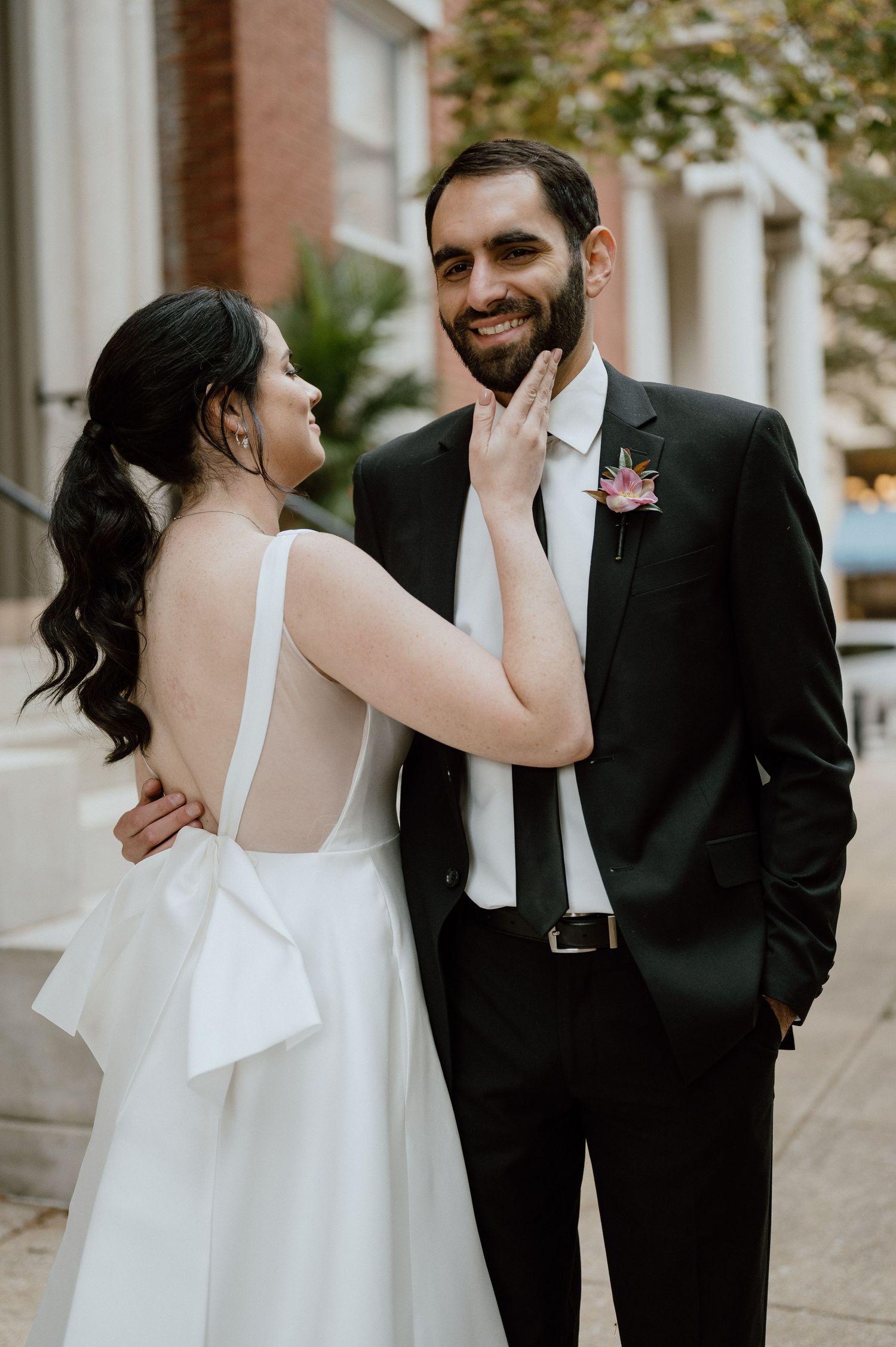A tender moment between newlyweds on a city street with classic architecture in the background.