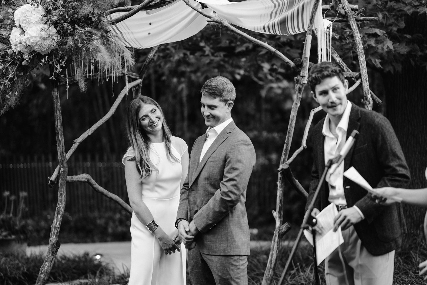 Black and white capture of a wedding ceremony beneath a rustic wooden canopy.