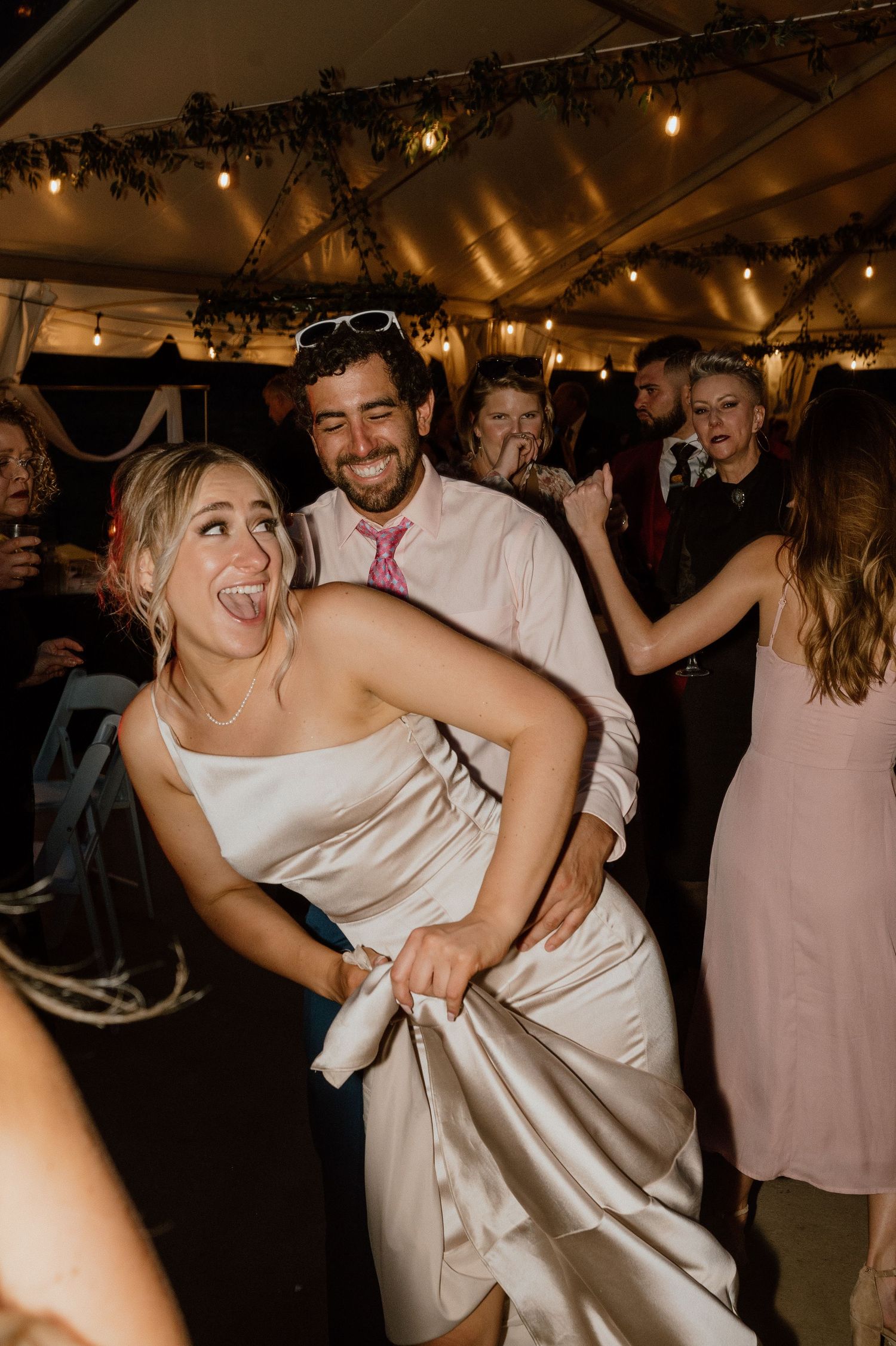 Joyful dancing and celebration at a wedding reception under decorated tent lighting.