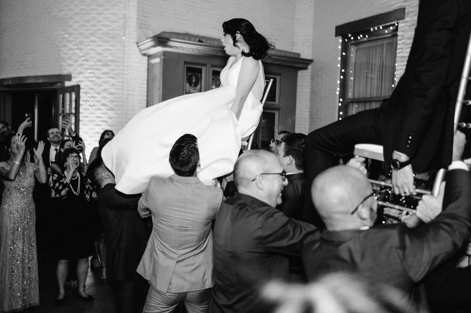 Wedding guests lift someone in a white dress during an energetic dance celebration.