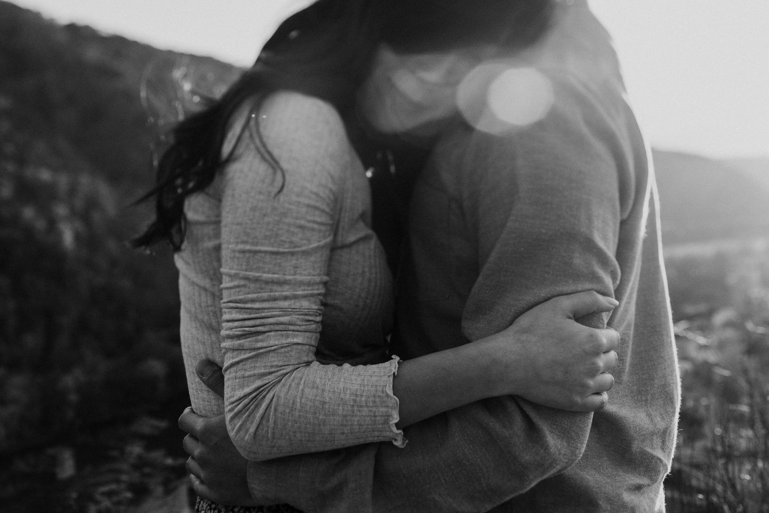 Black and white intimate portrait of couple embracing on hillside.