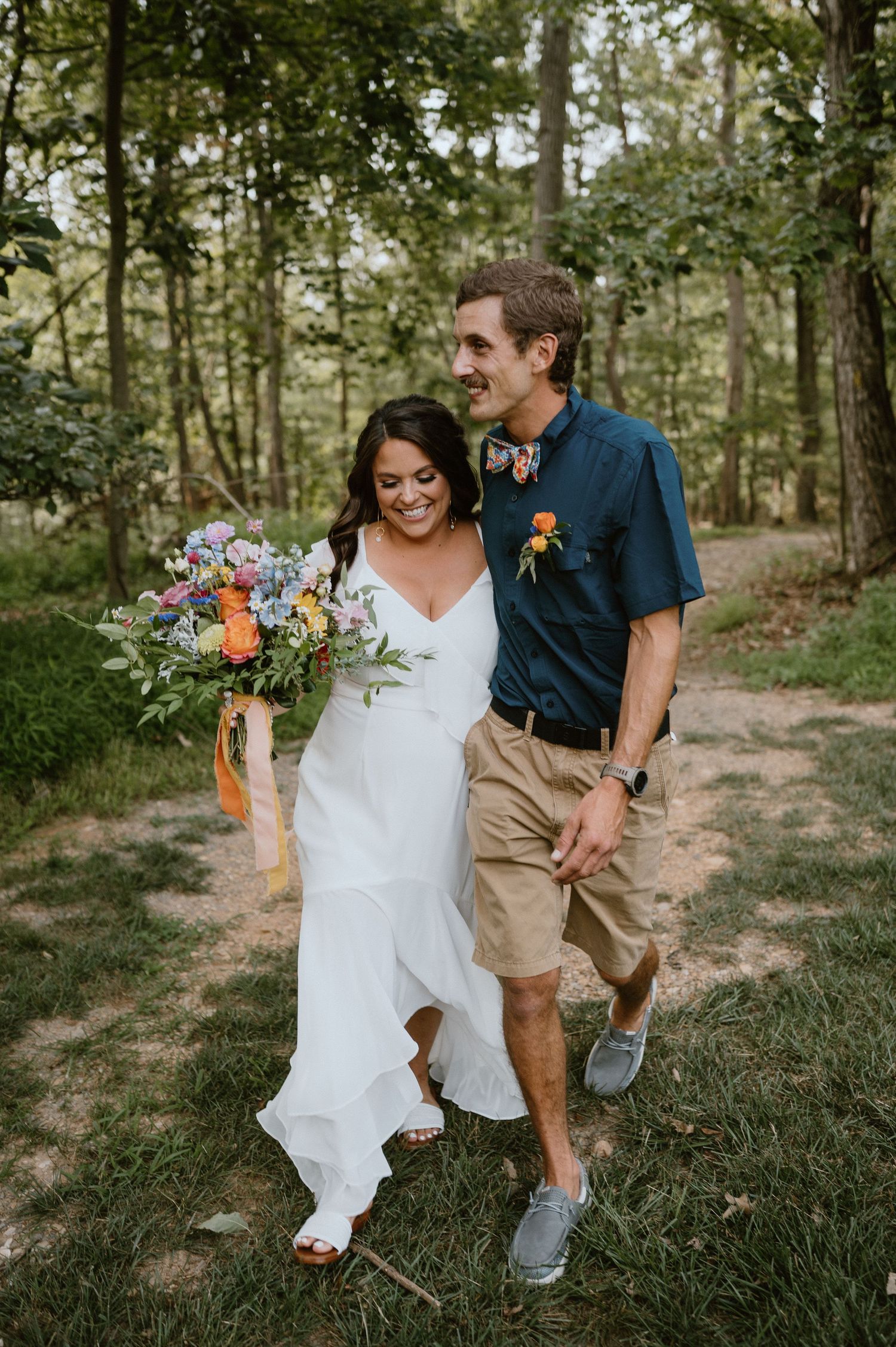 A joyful couple walking together outdoors, the bride holding a colorful wildflower bouquet.