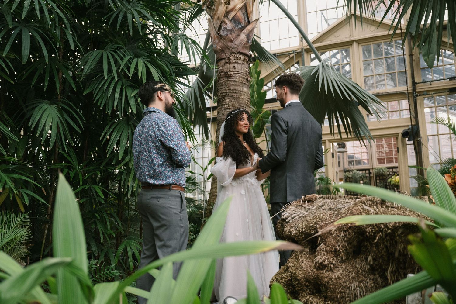 Intimate wedding ceremony in a greenhouse surrounded by tropical plants and natural light.