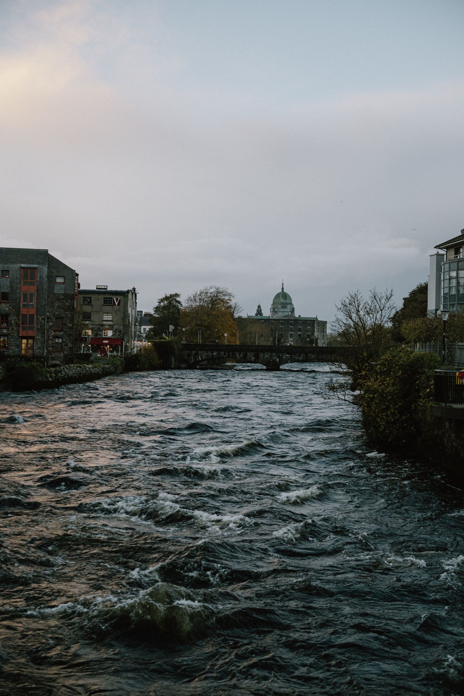 Rushing river through city center with historic buildings and dome visible in background.