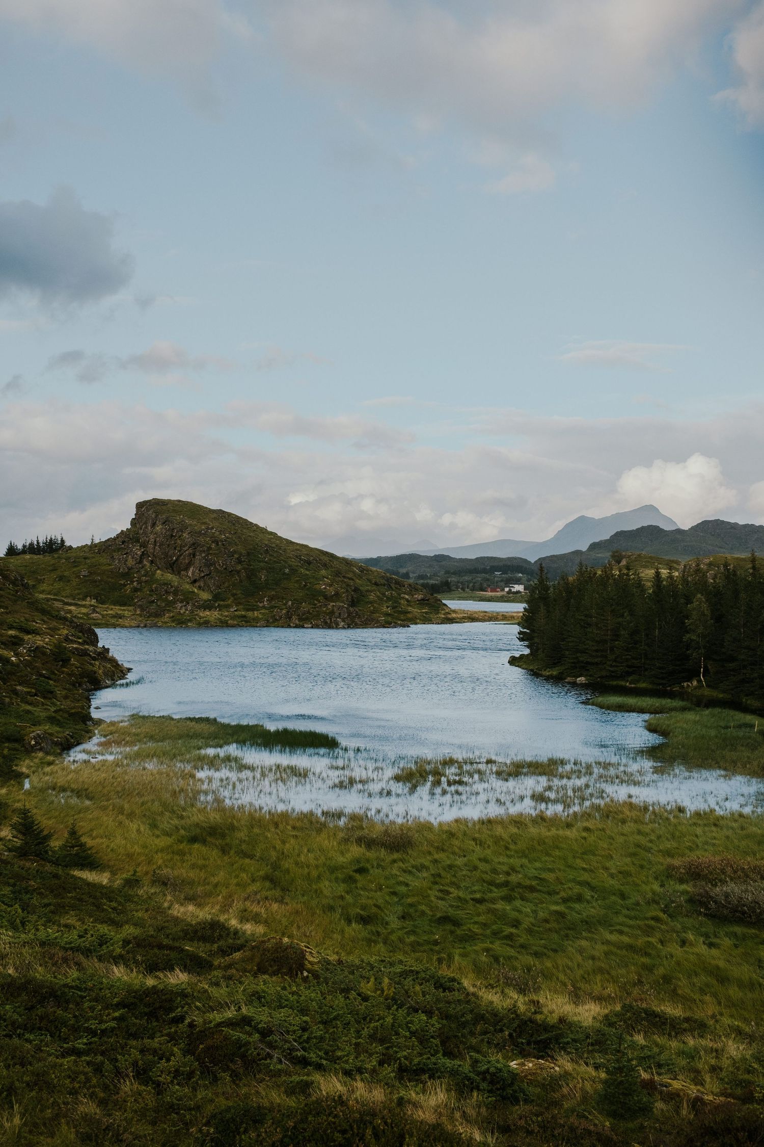 Scenic lake surrounded by rolling hills and evergreen forests in a remote wilderness landscape.