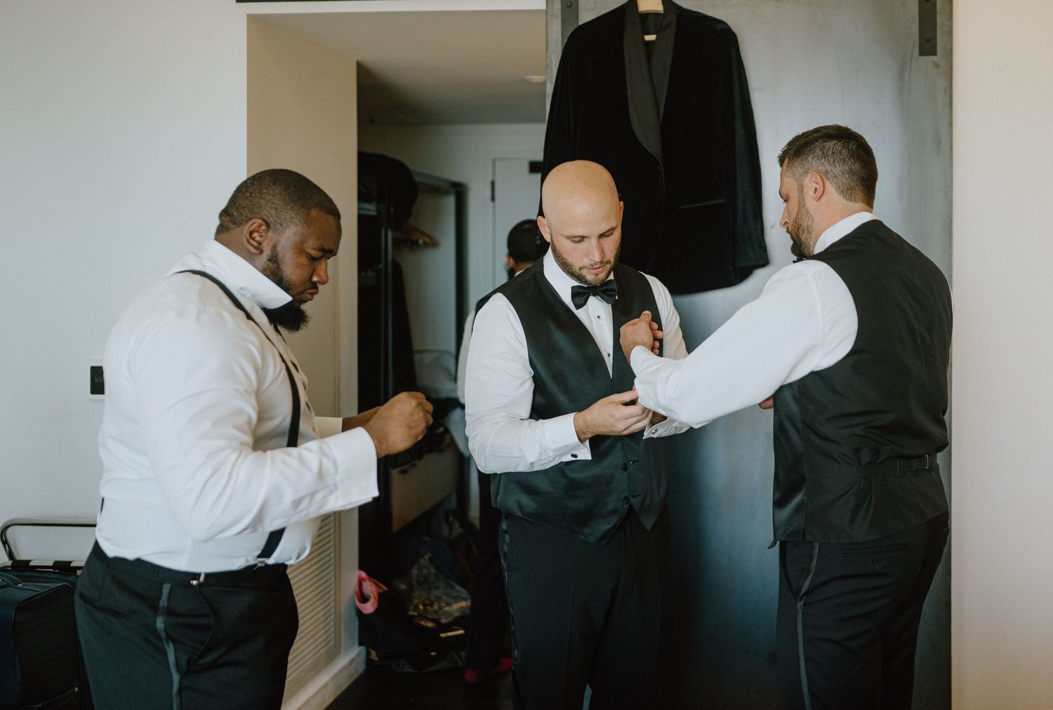 Groomsmen help adjust formal wear and ties while getting ready for a wedding.
