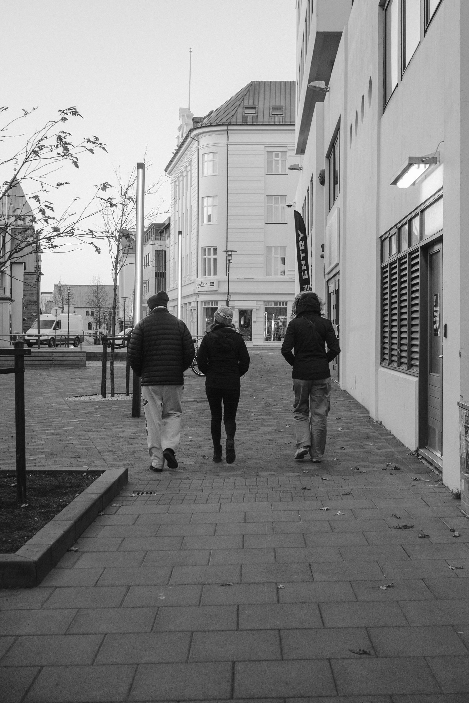 Three people walking down an urban sidewalk in black and white.