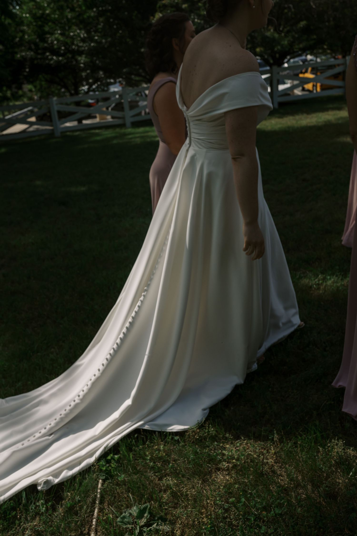 Close-up detail of white wedding dress train with buttons trailing on grass.
