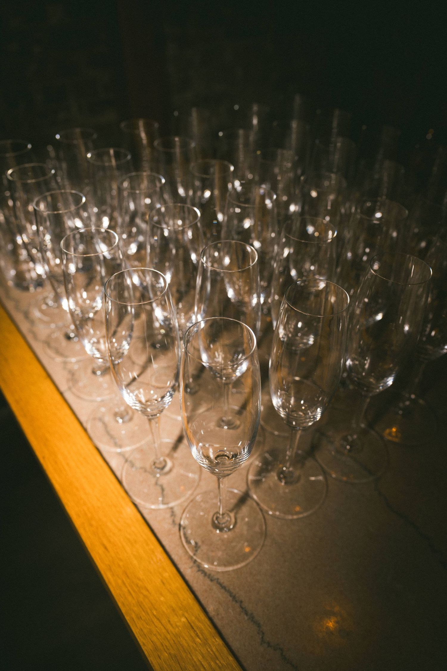 Rows of empty champagne glasses lined up on a wooden table.