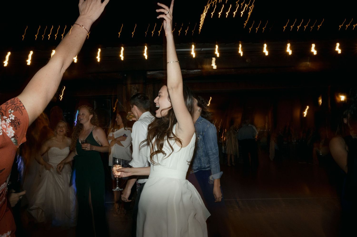 A wedding celebration in a dimly lit venue with dancing and raised arms.