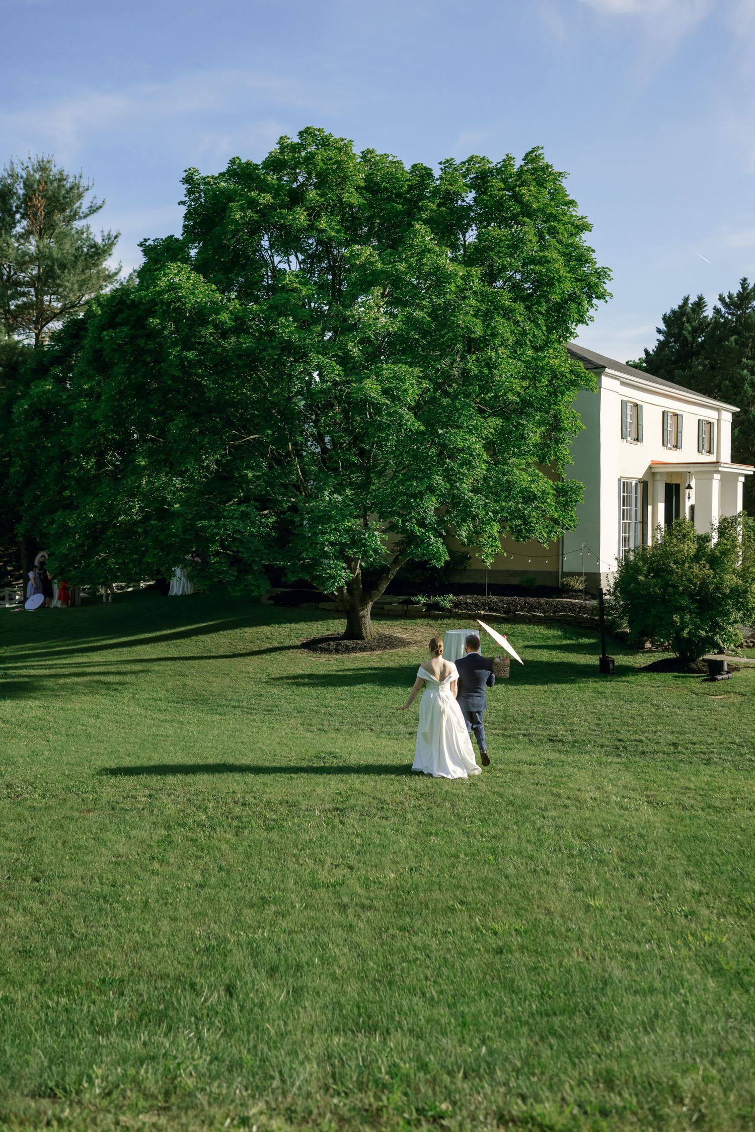 A wedding scene on a vast lawn with a white colonial house in the background.