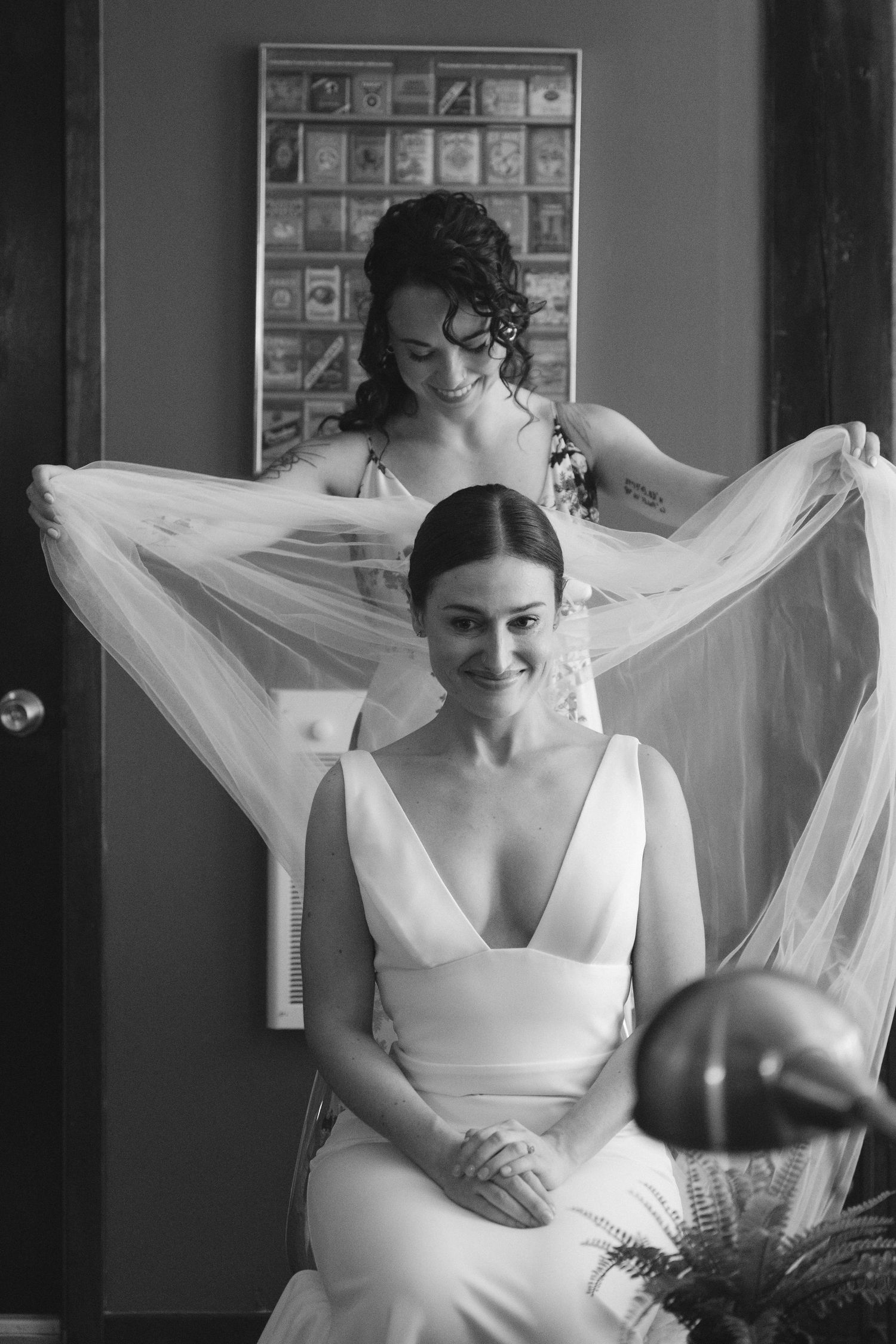A black and white photo capturing an intimate wedding preparation moment with a flowing veil.