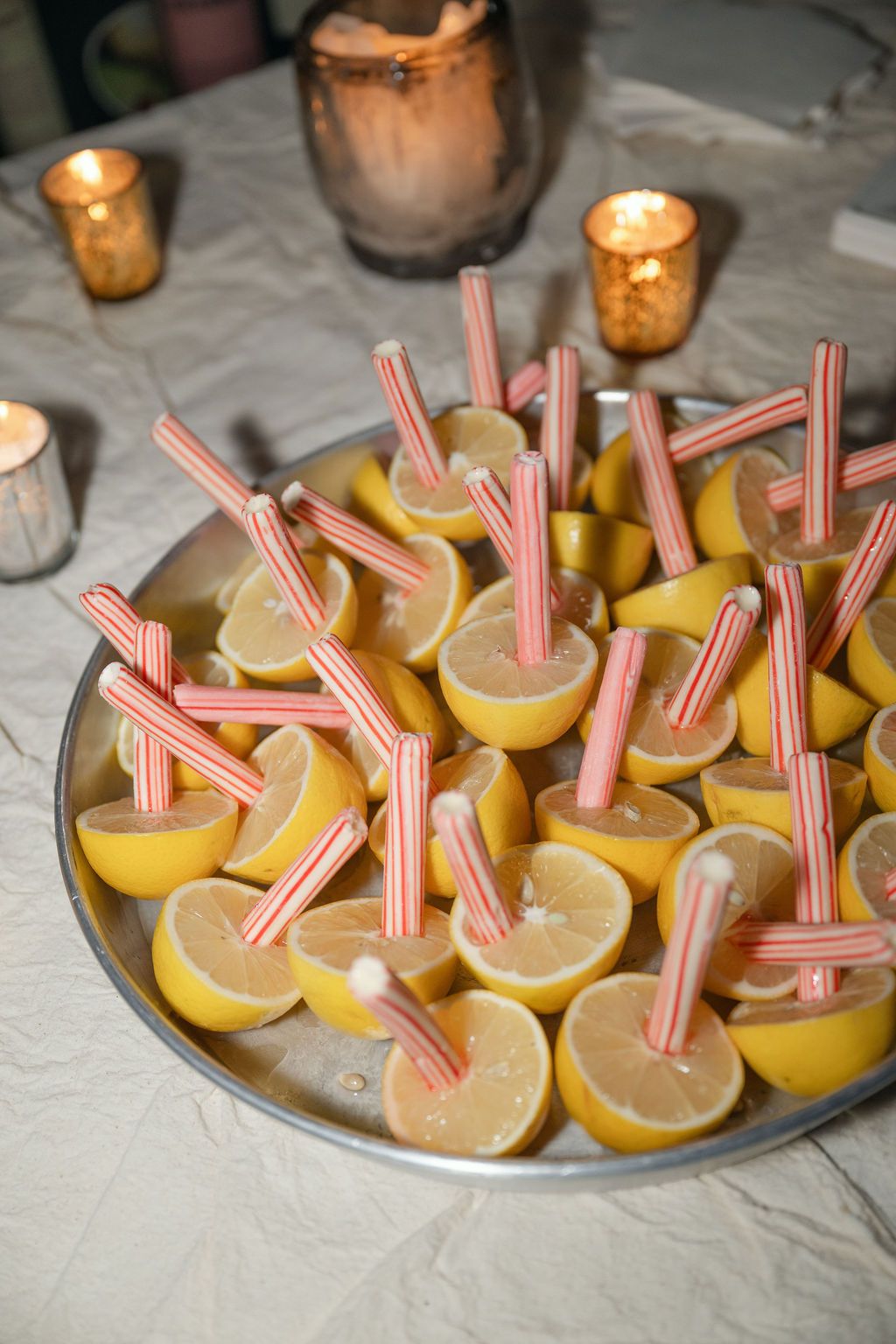 Lemon slices garnished with pink striped straws arranged on a silver platter with glowing candles in the background Fadensonnon in Baltimore