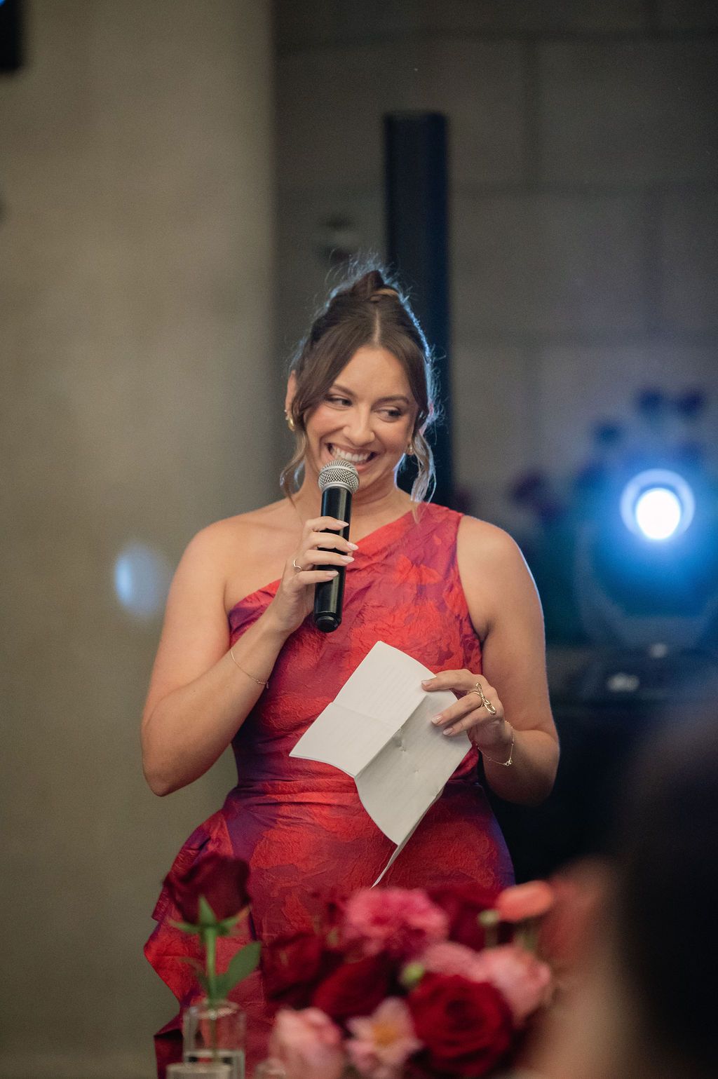 Person in a red formal dress holds up papers while speaking emotionally at a podium during an event.