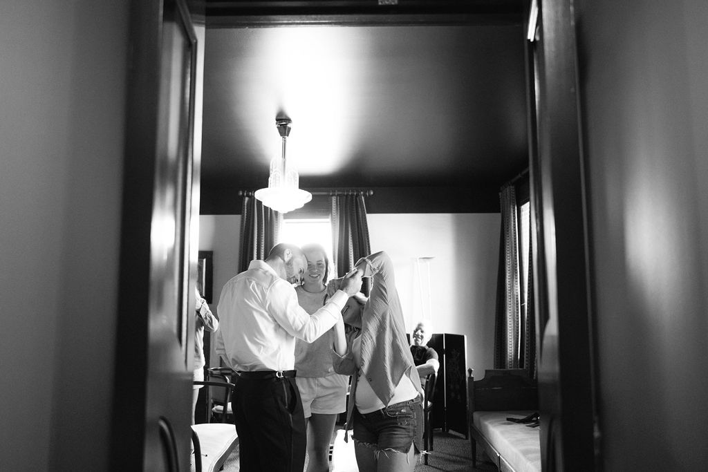 Black and white photo of people getting ready in a hallway with chandelier lighting.