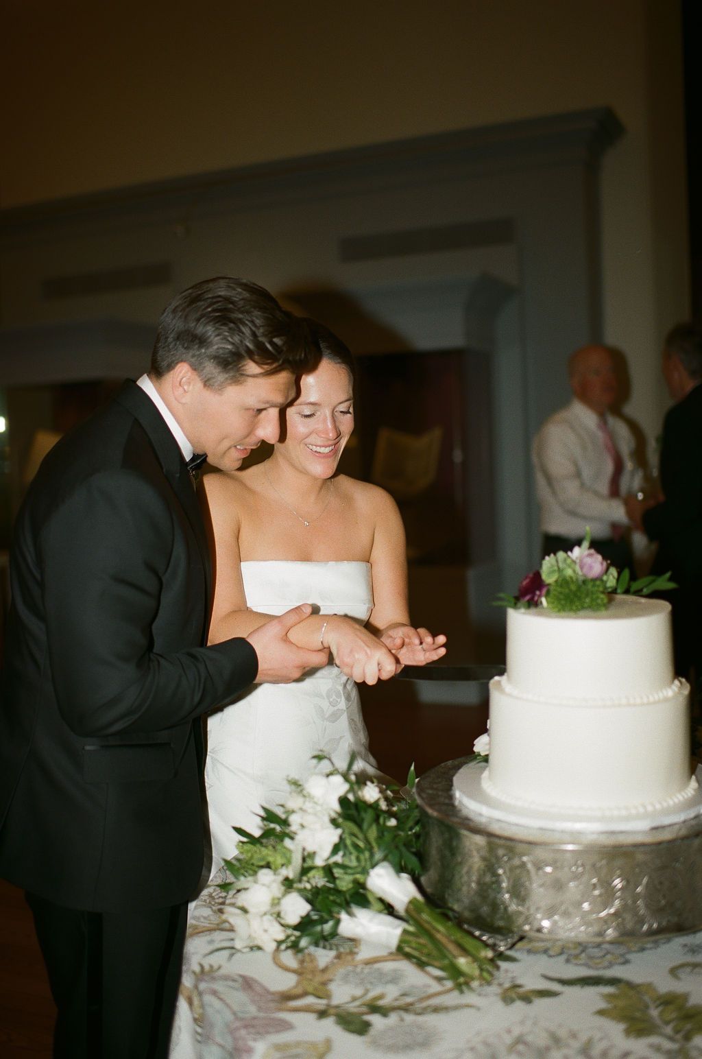Couple cutting their white wedding cake decorated with flowers at the reception at George Peabody Library Wedding in Baltimore