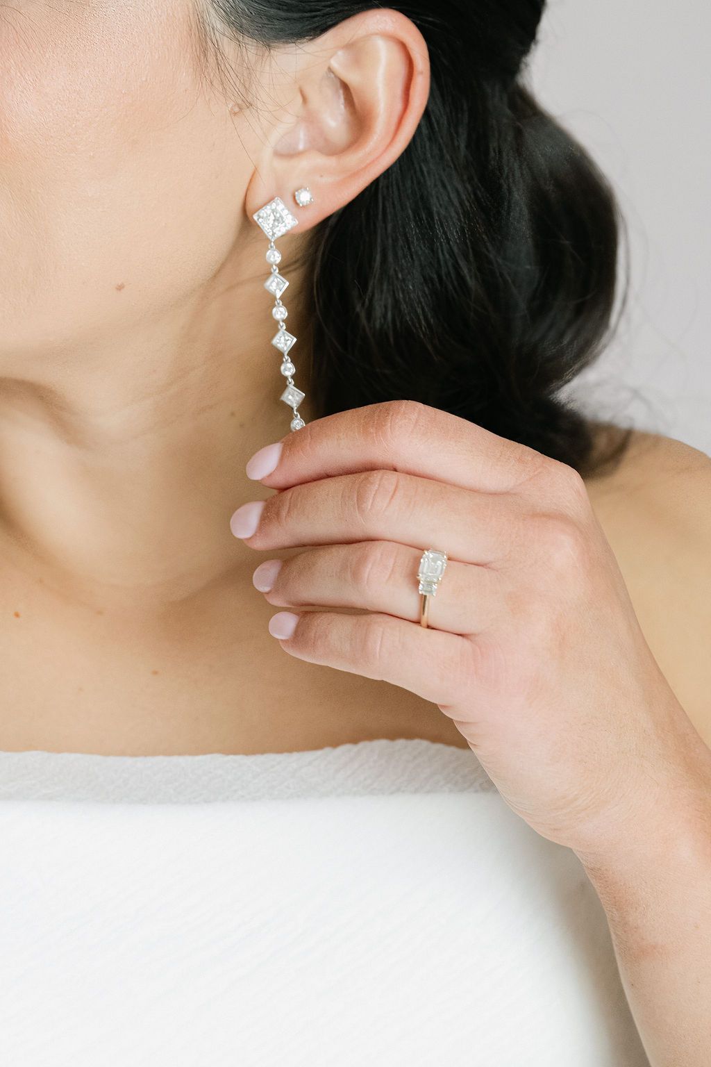 Elegant diamond drop earrings and wedding ring displayed on a light background.
