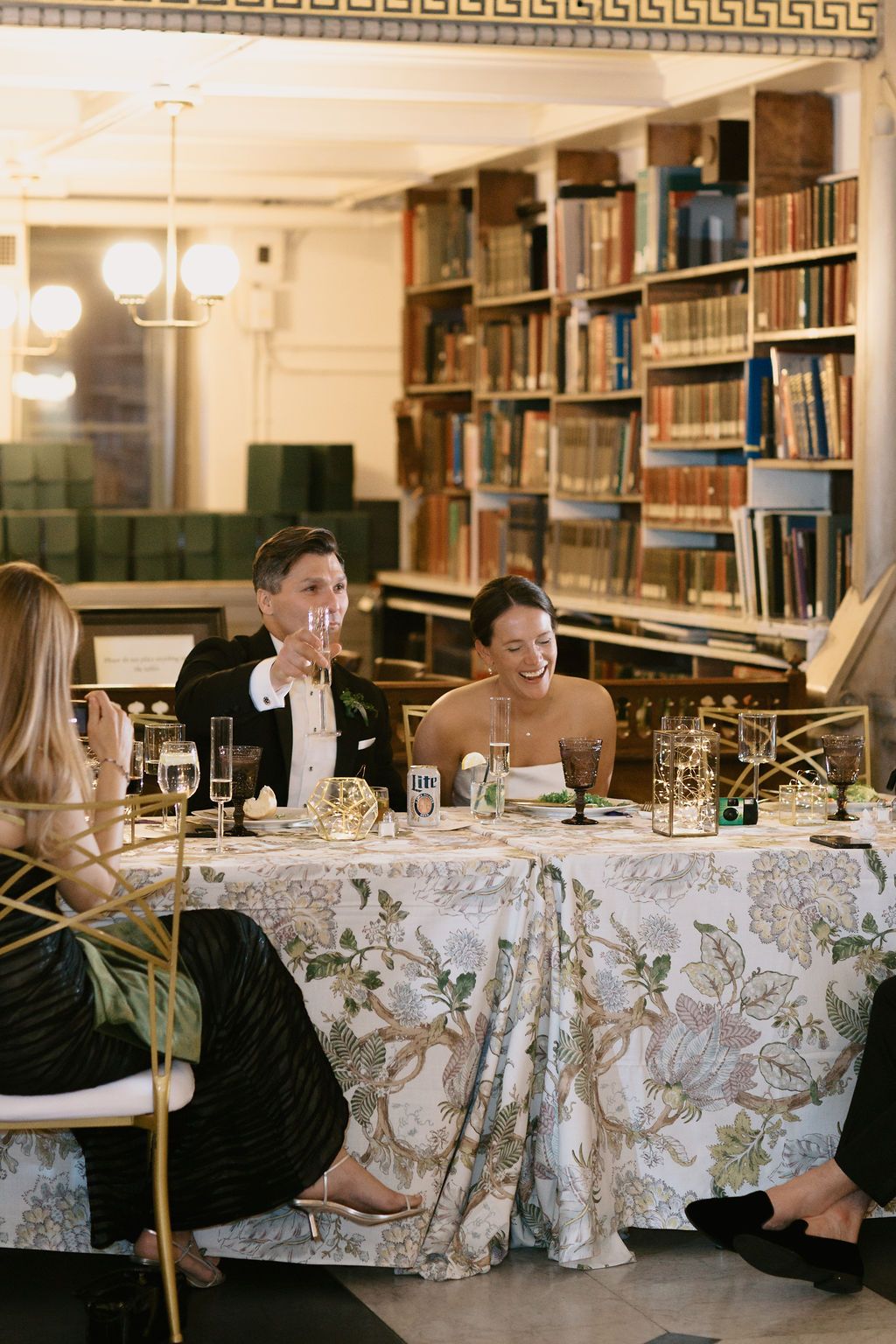 Wedding guests seated at tables in a library setting with ornate decor and bookshelves at George Peabody Library Wedding in Baltimore