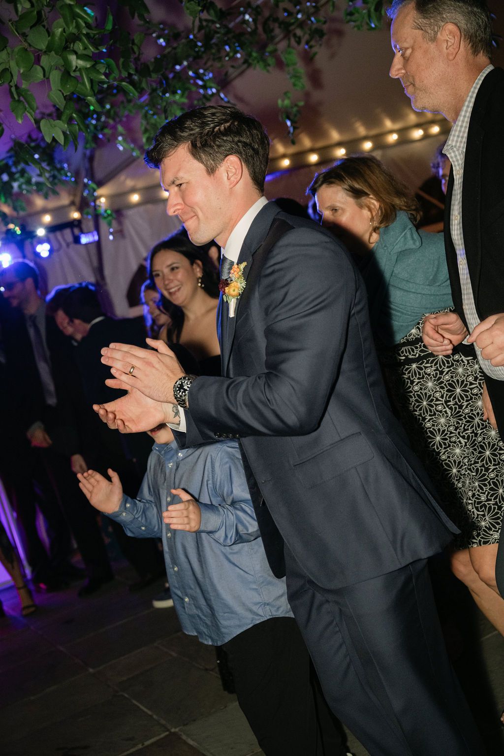 Guests dance and celebrate at an evening wedding reception decorated with purple lighting and greenery