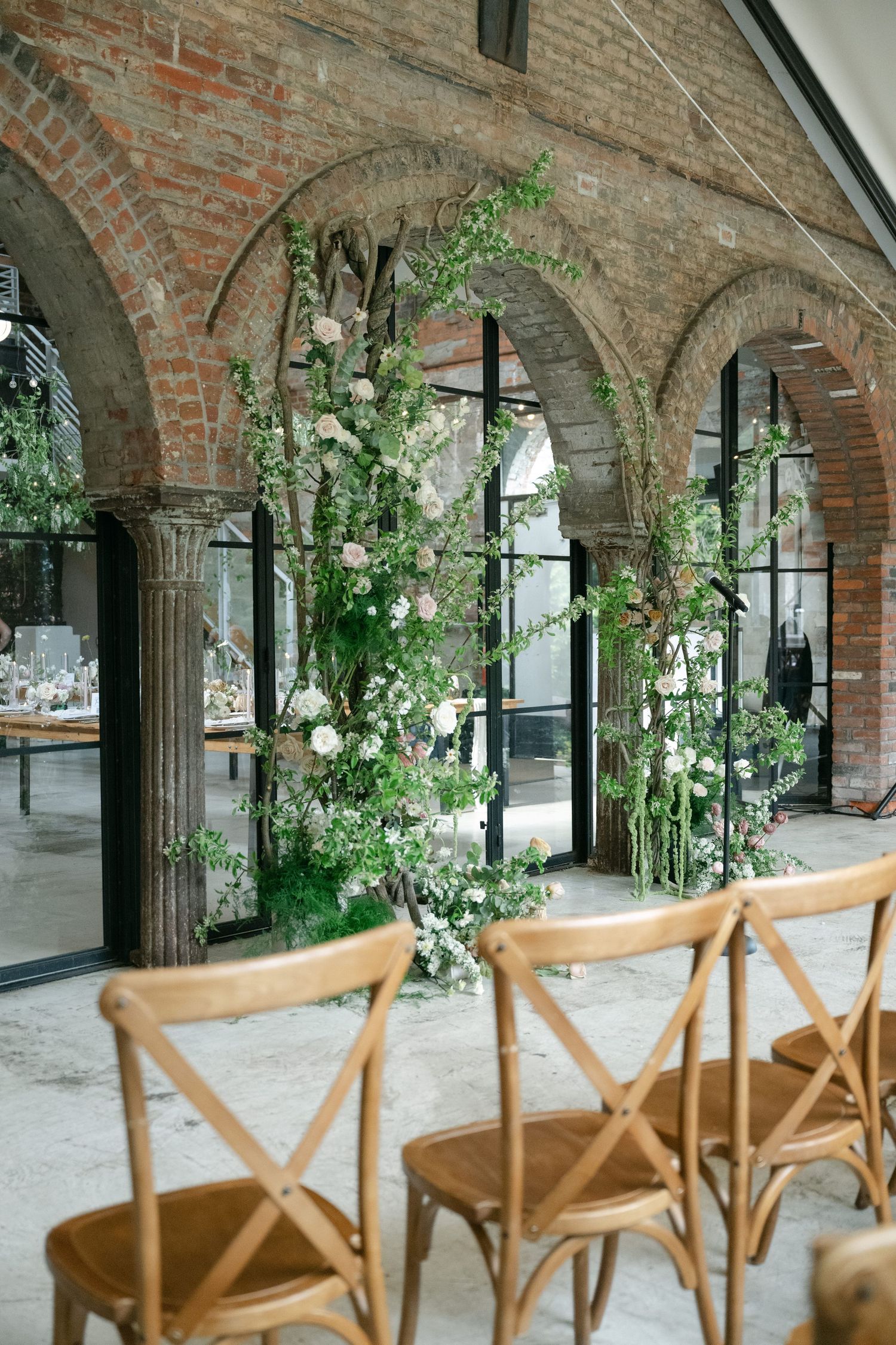 Wedding ceremony setup with wooden chairs and floral arch in a brick archway venue.