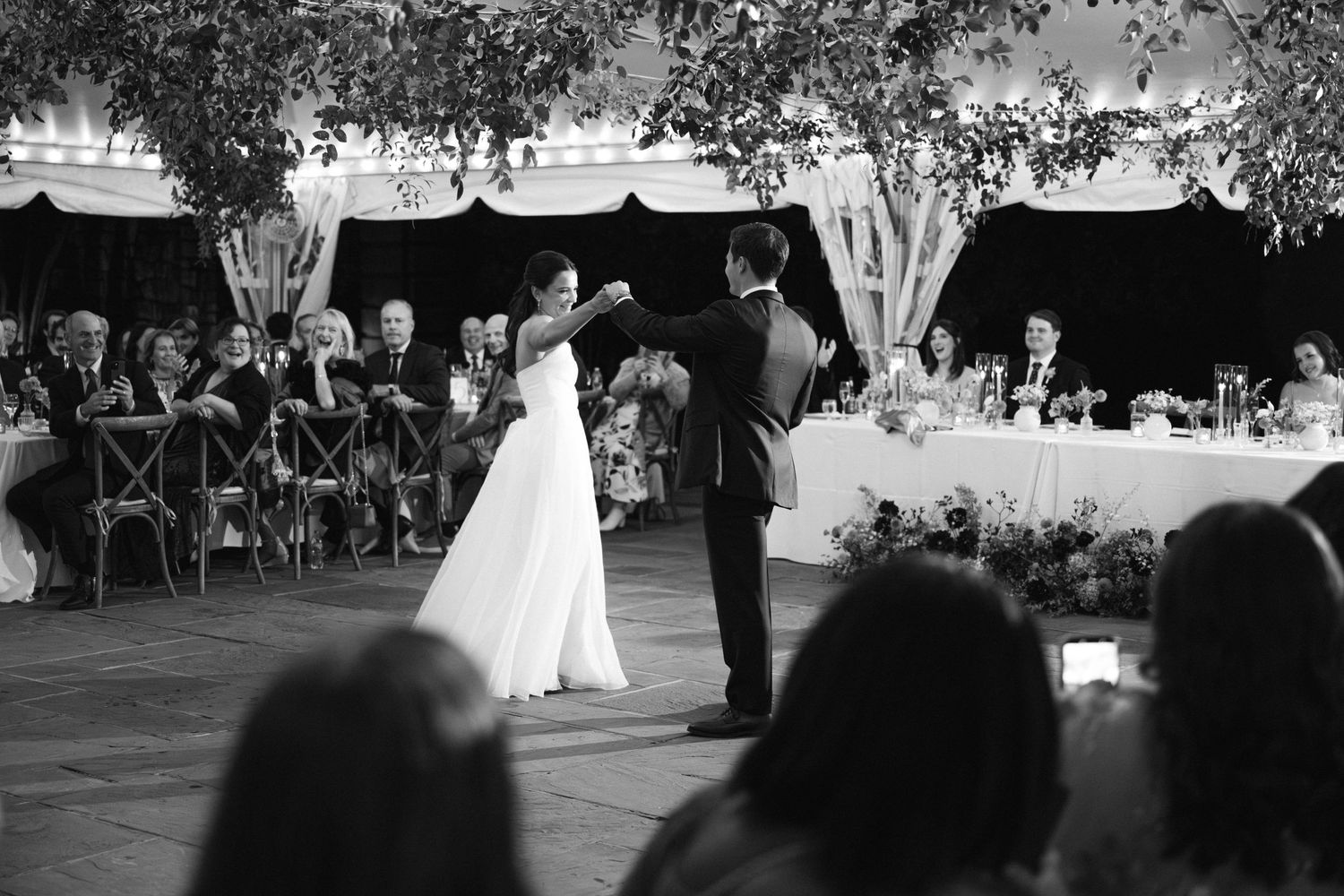 An outdoor wedding reception with guests seated under trees at dusk.