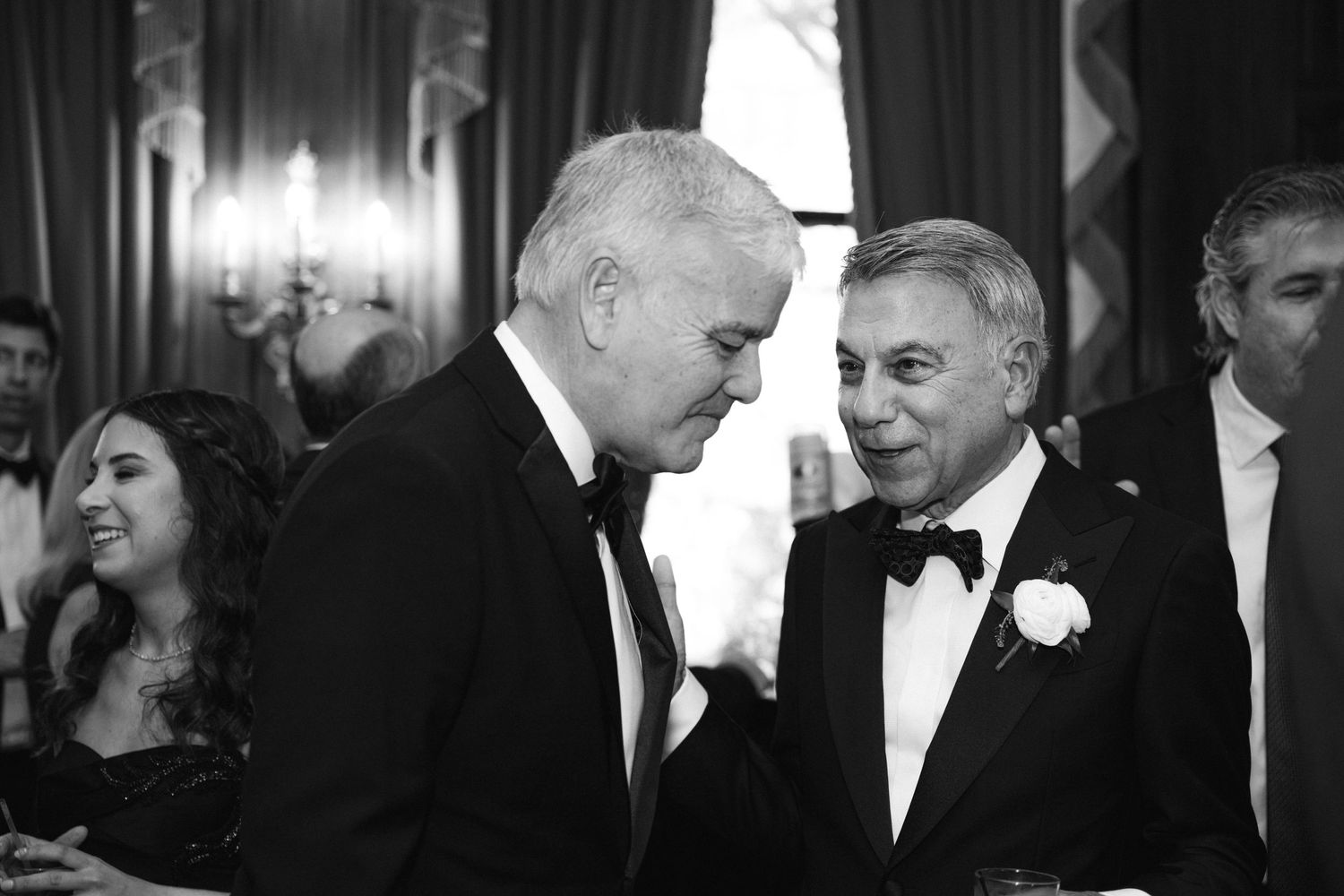Two men in tuxedos having an animated conversation at a formal event.