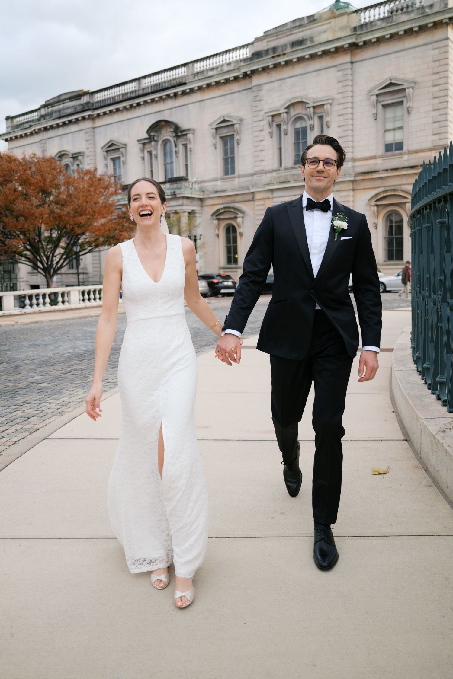 Newlyweds walking and laughing together outside a grand historic building.