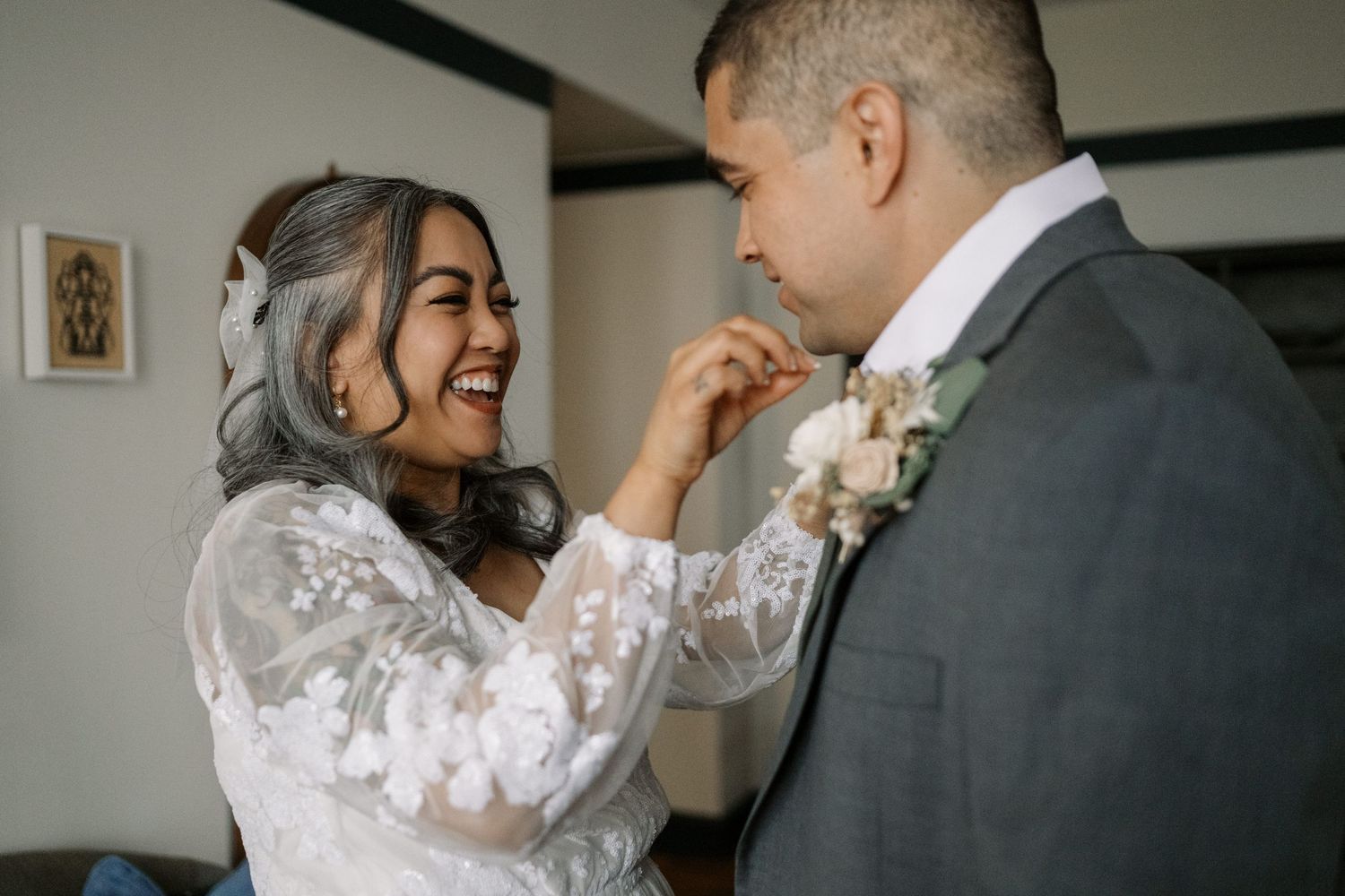 A joyful candid moment shared between a couple at a wedding, with the bride in a lace dress and groom in a gray suit.