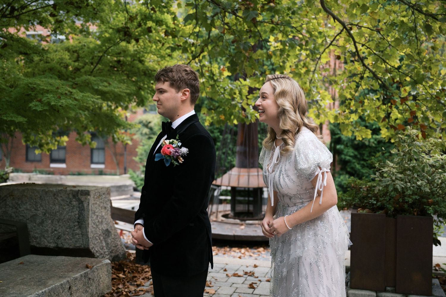 A wedding couple stands together under green trees during their outdoor ceremony.