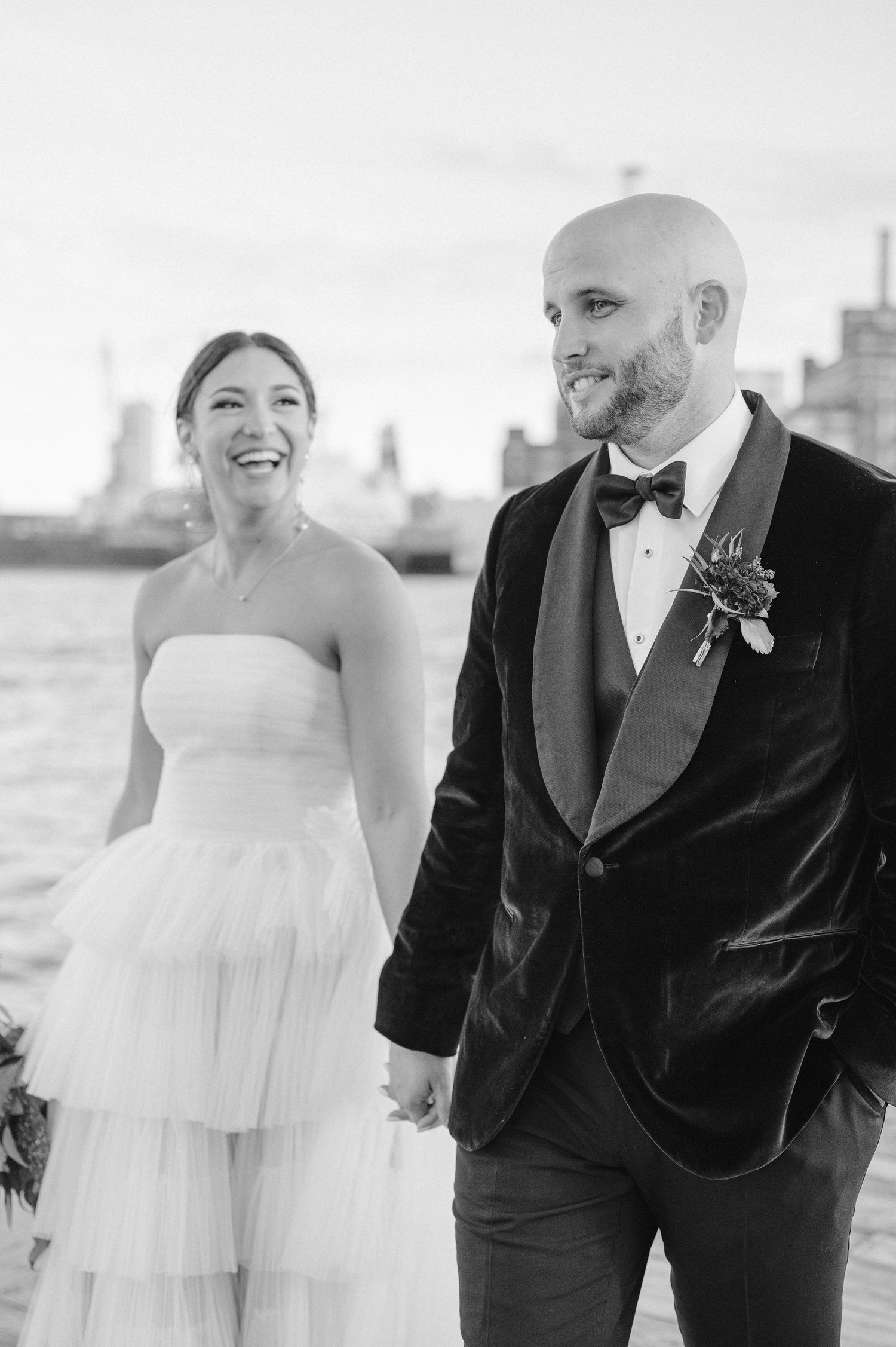 Black and white wedding portrait of a couple laughing together on a waterfront.