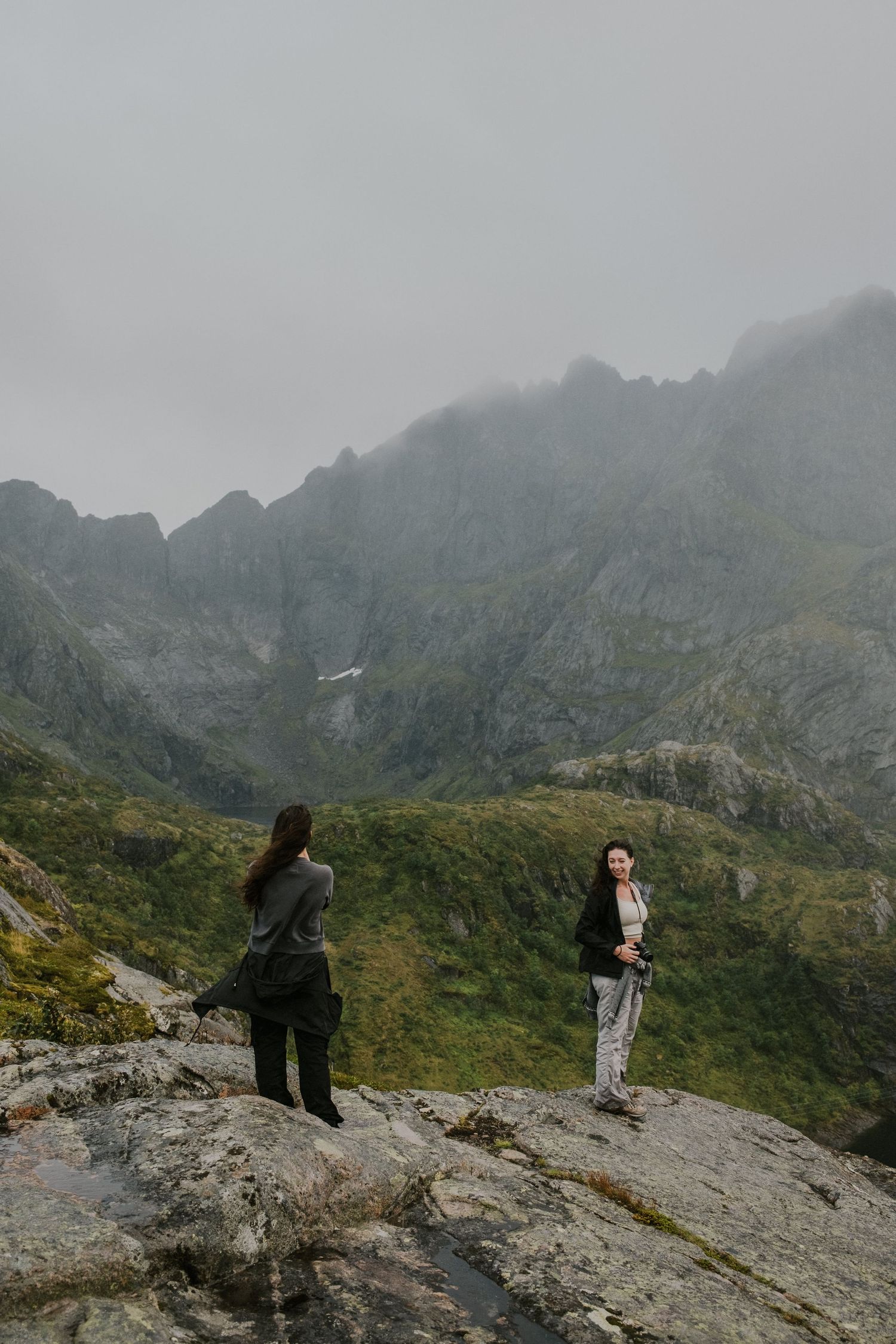 Hikers enjoying dramatic mountain views from a rocky outcrop in misty conditions.