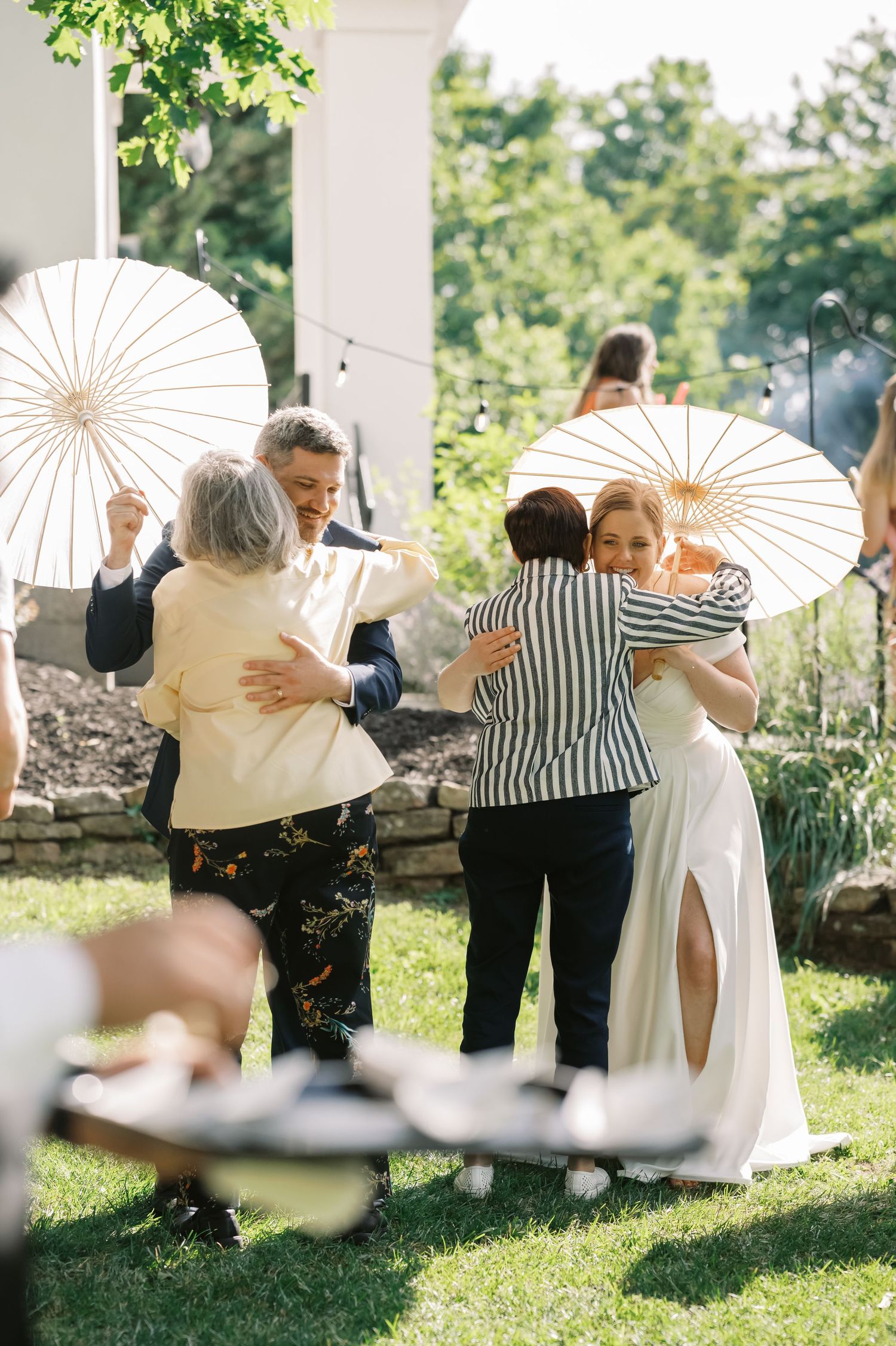 Wedding celebration with white parasols in a sunny garden setting.
