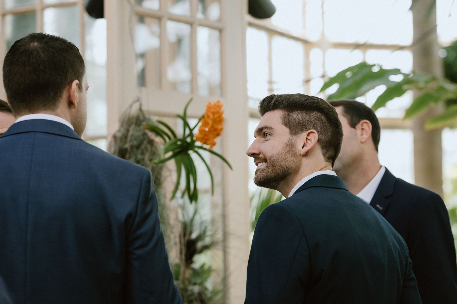 Guests gather in a bright conservatory with tropical plants during an event.